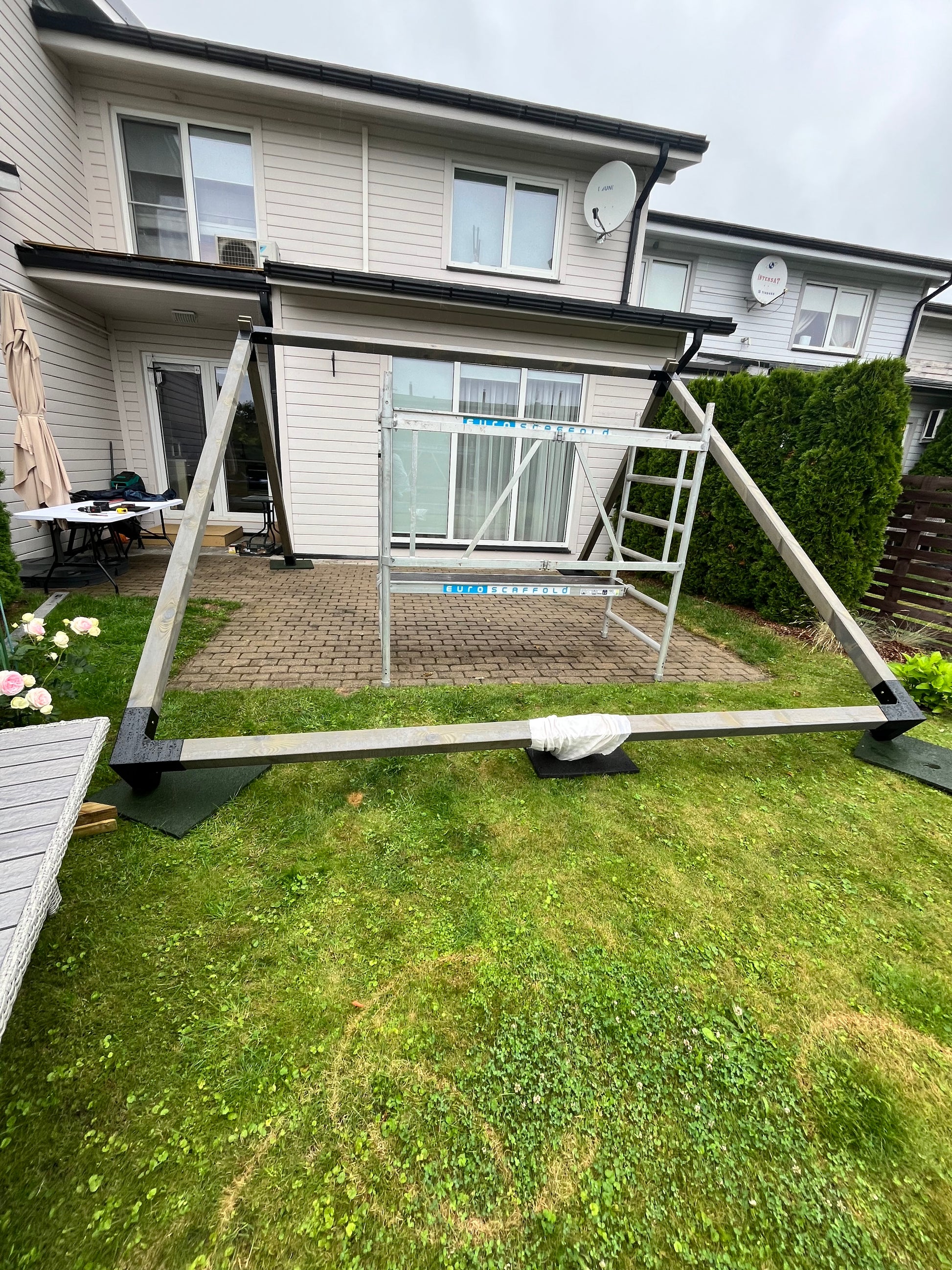 Outdoor patio area with a pergola attached to a house, featuring grass and a small garden.