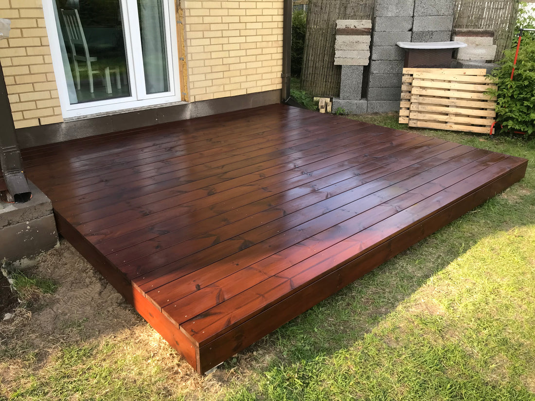 Wooden deck extending from a house with grass and building materials in the background