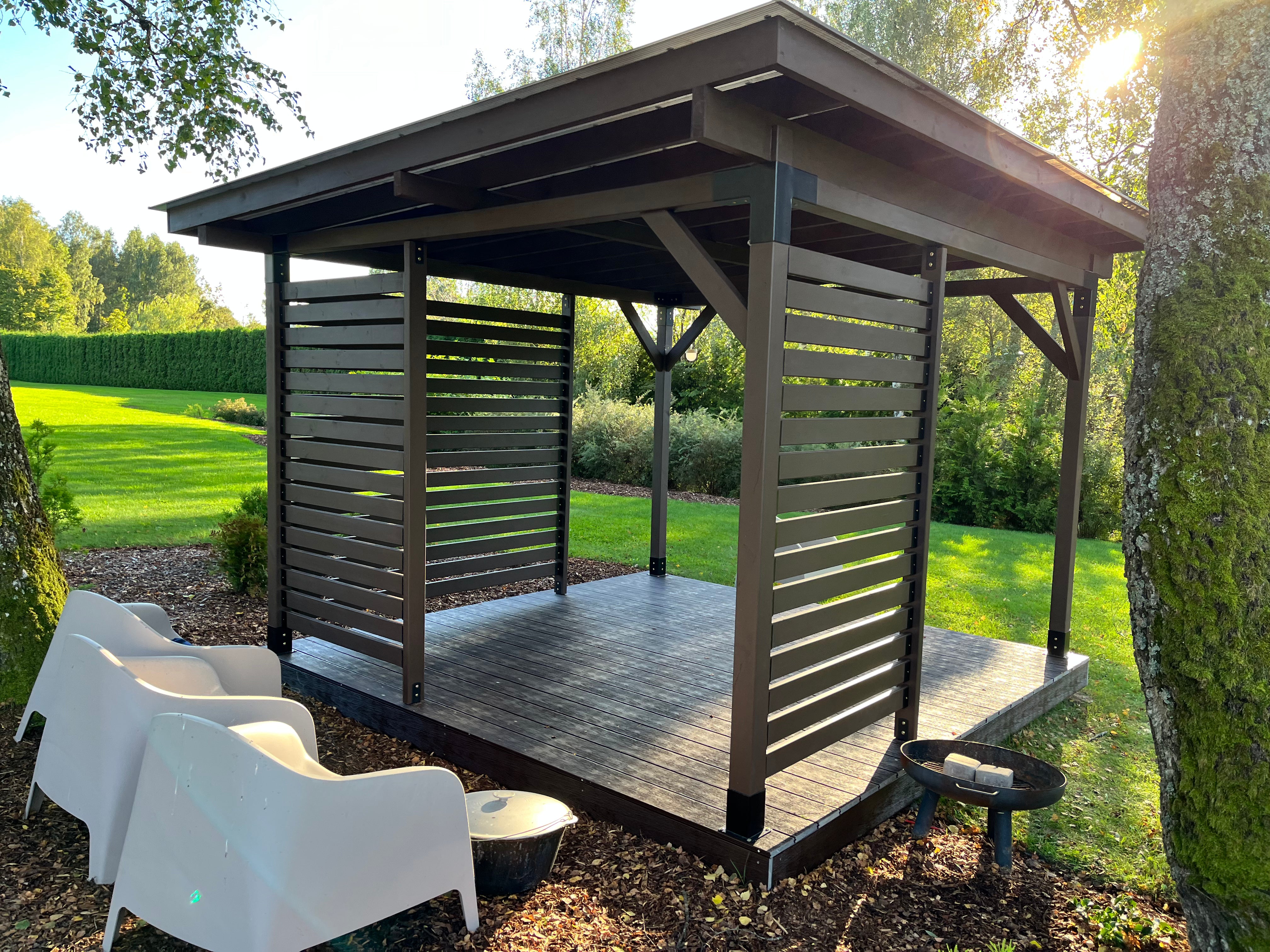 Wooden outdoor gazebo with chairs and a fire pit in a garden setting