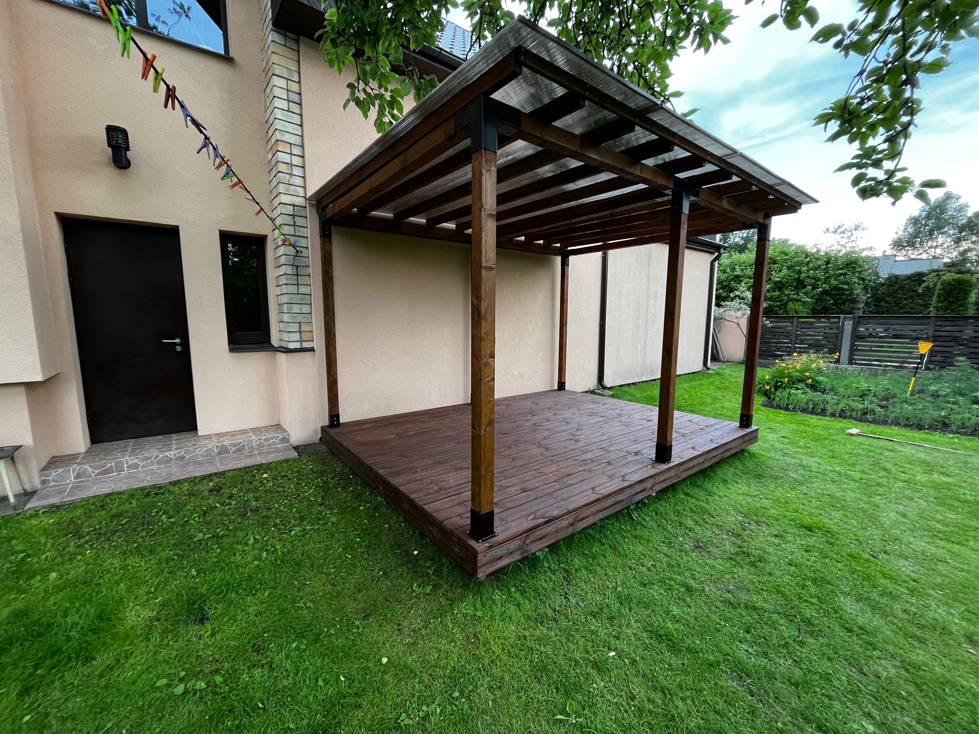 Wooden pergola in a backyard with grass and a house in the background