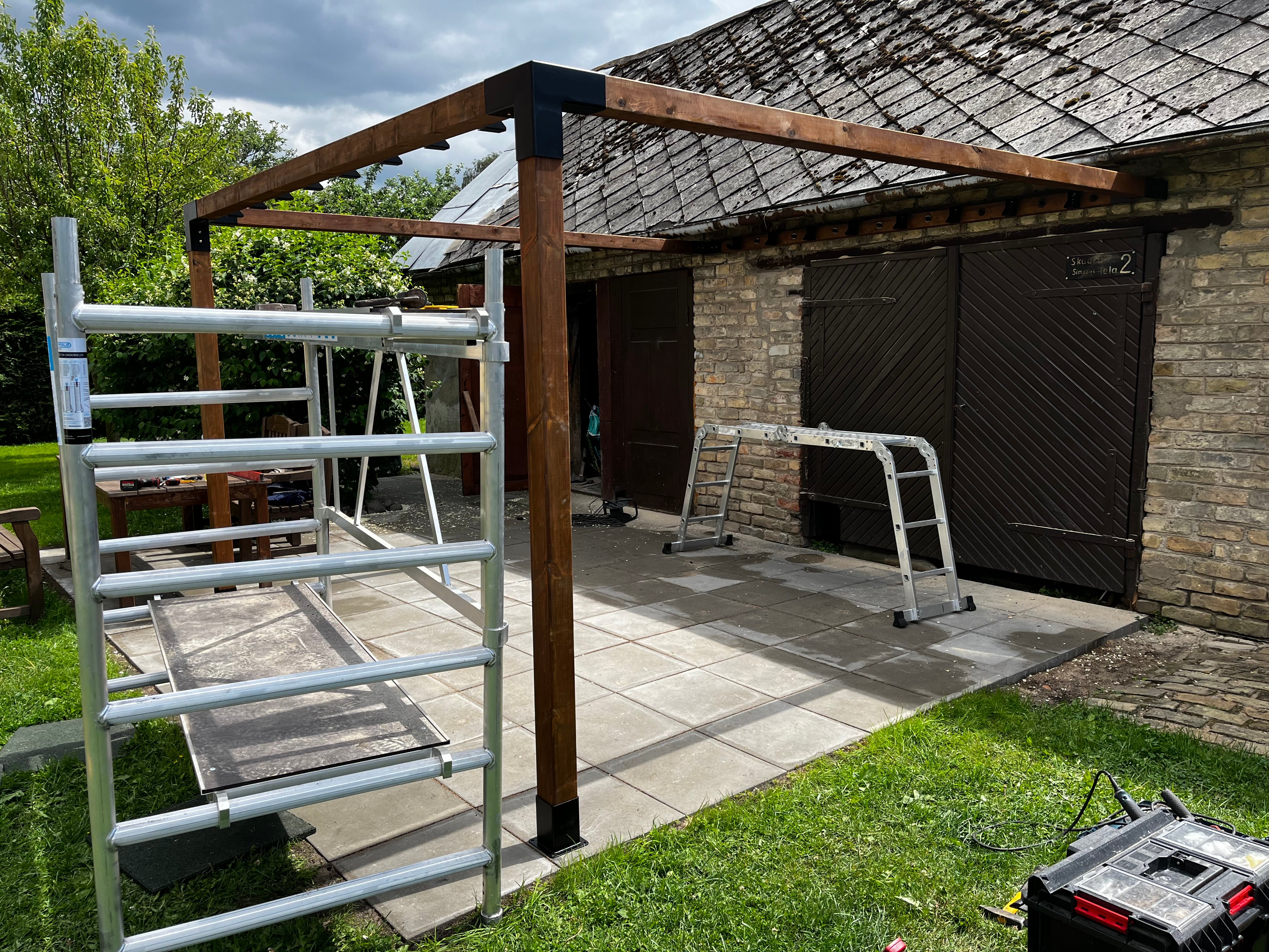 Outdoor construction site with wooden frame and metal ladders near a building.