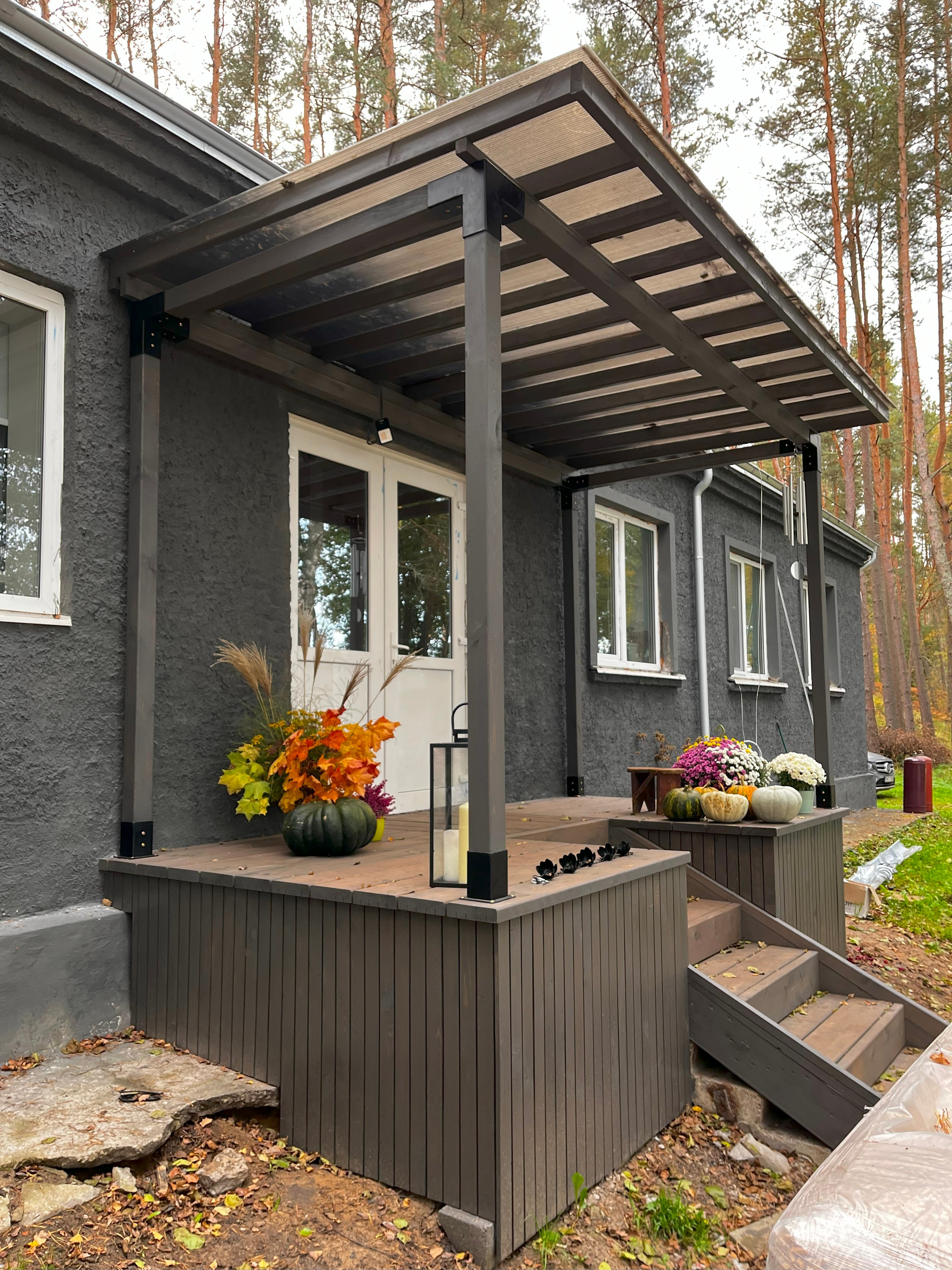 Patio with wooden pergola, flowers, and lanterns in front of a house.