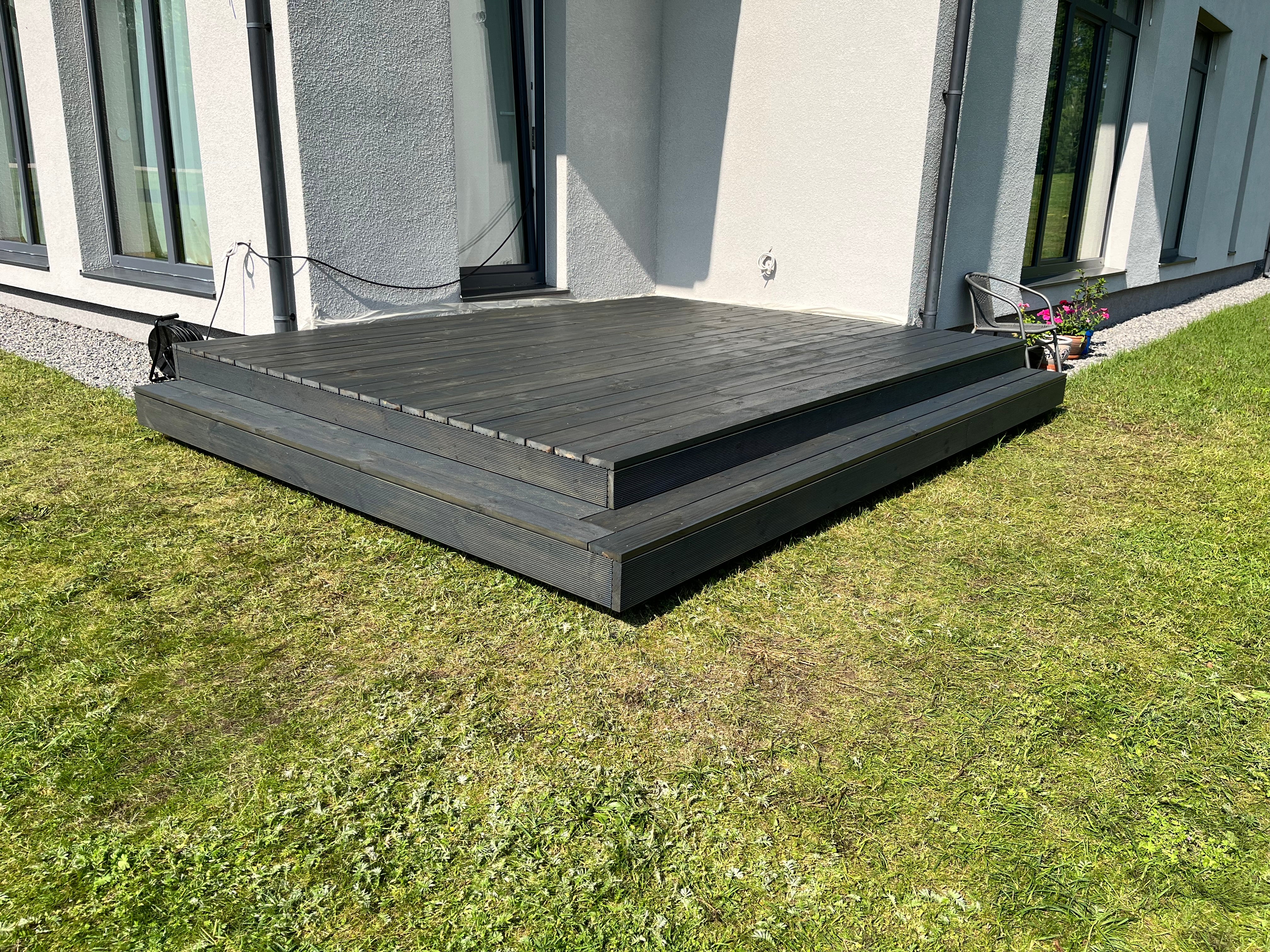 Wooden deck in front of a modern house with grass around