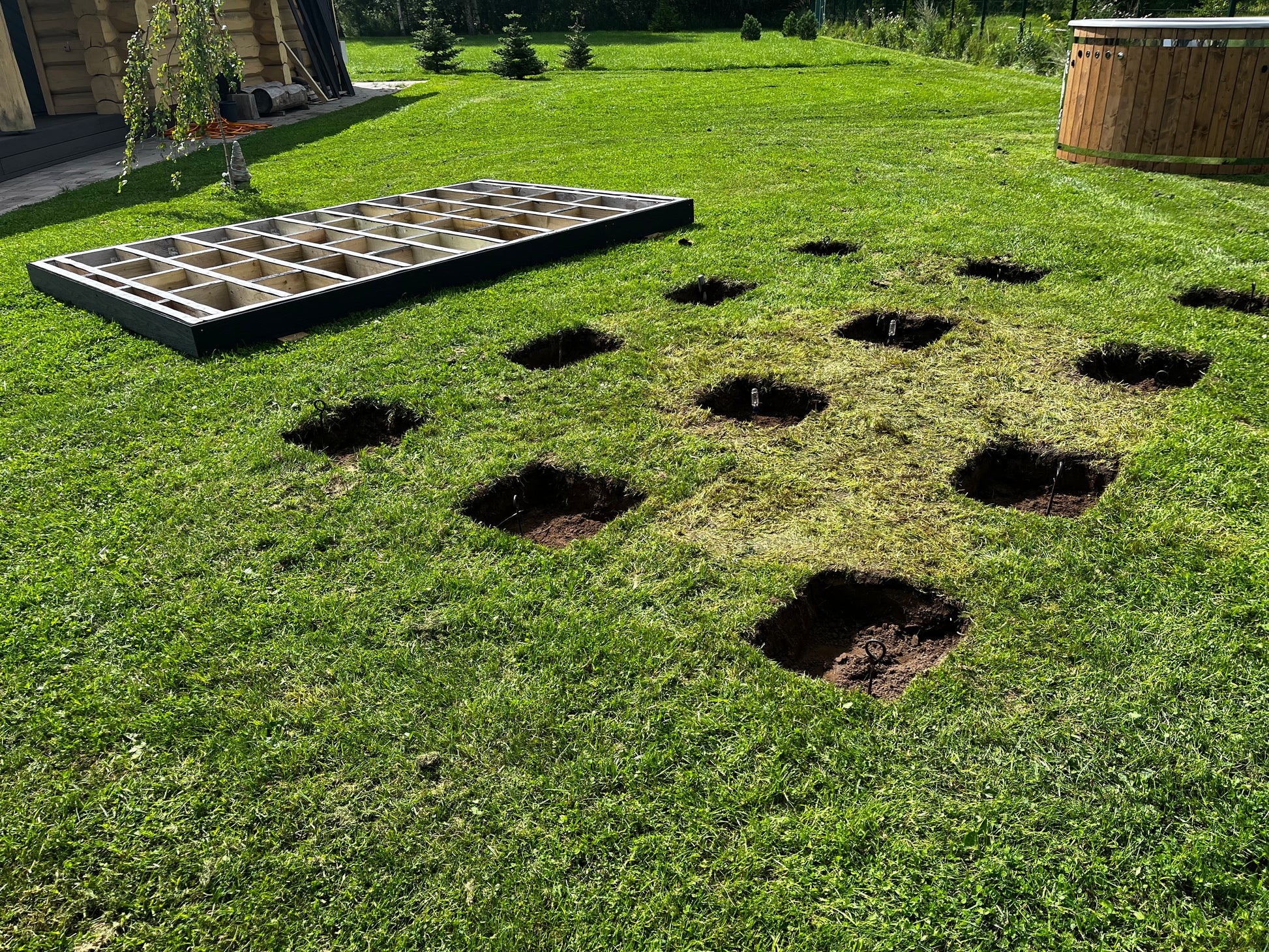 Garden bed with raised wooden frames and dug-out holes on a grassy area.