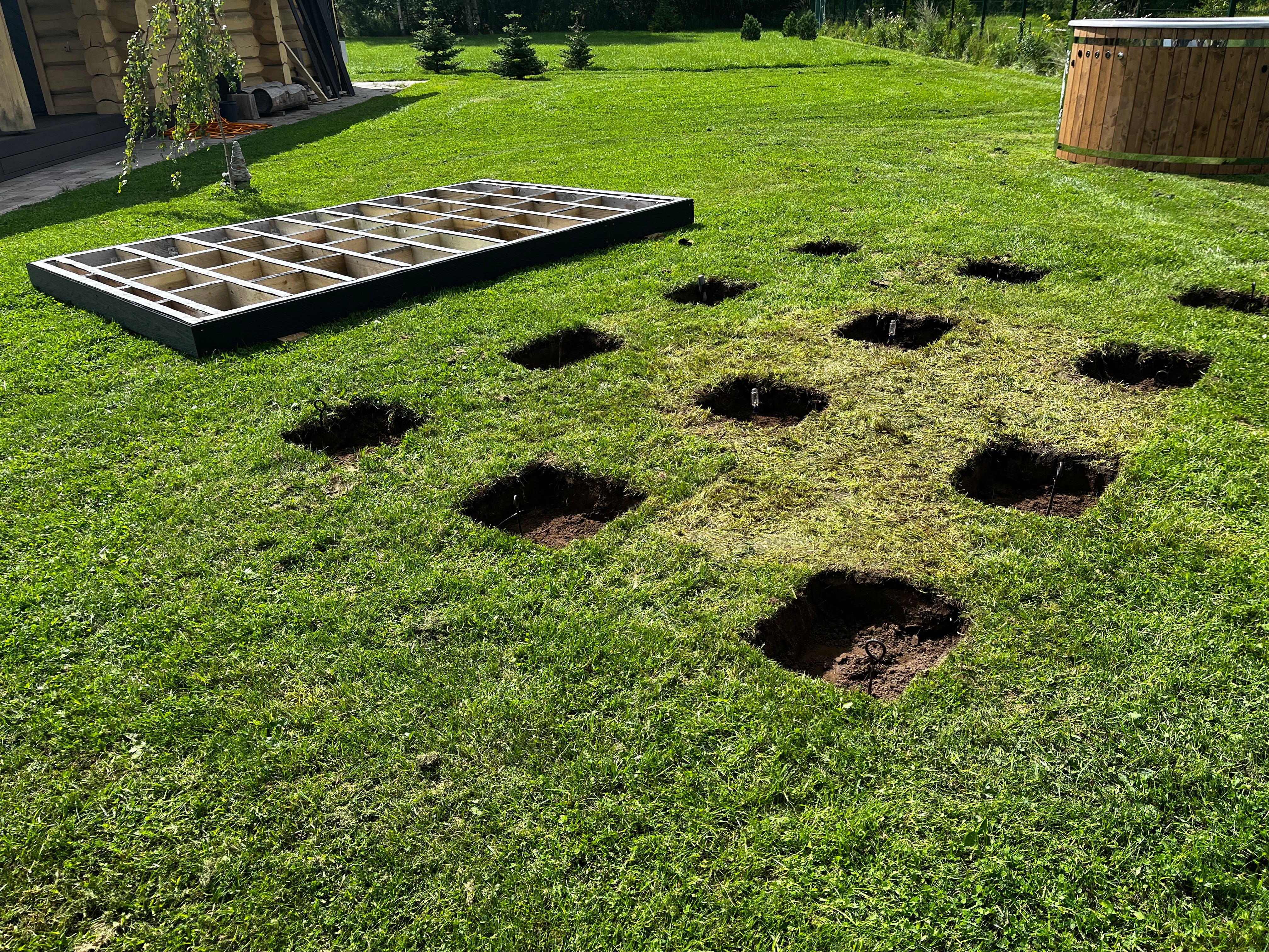 Garden bed with raised wooden frames and dug-out holes on a grassy area.