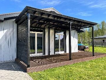 Wooden deck extension with pergola attached to a house, blue sky and green grass in the background
