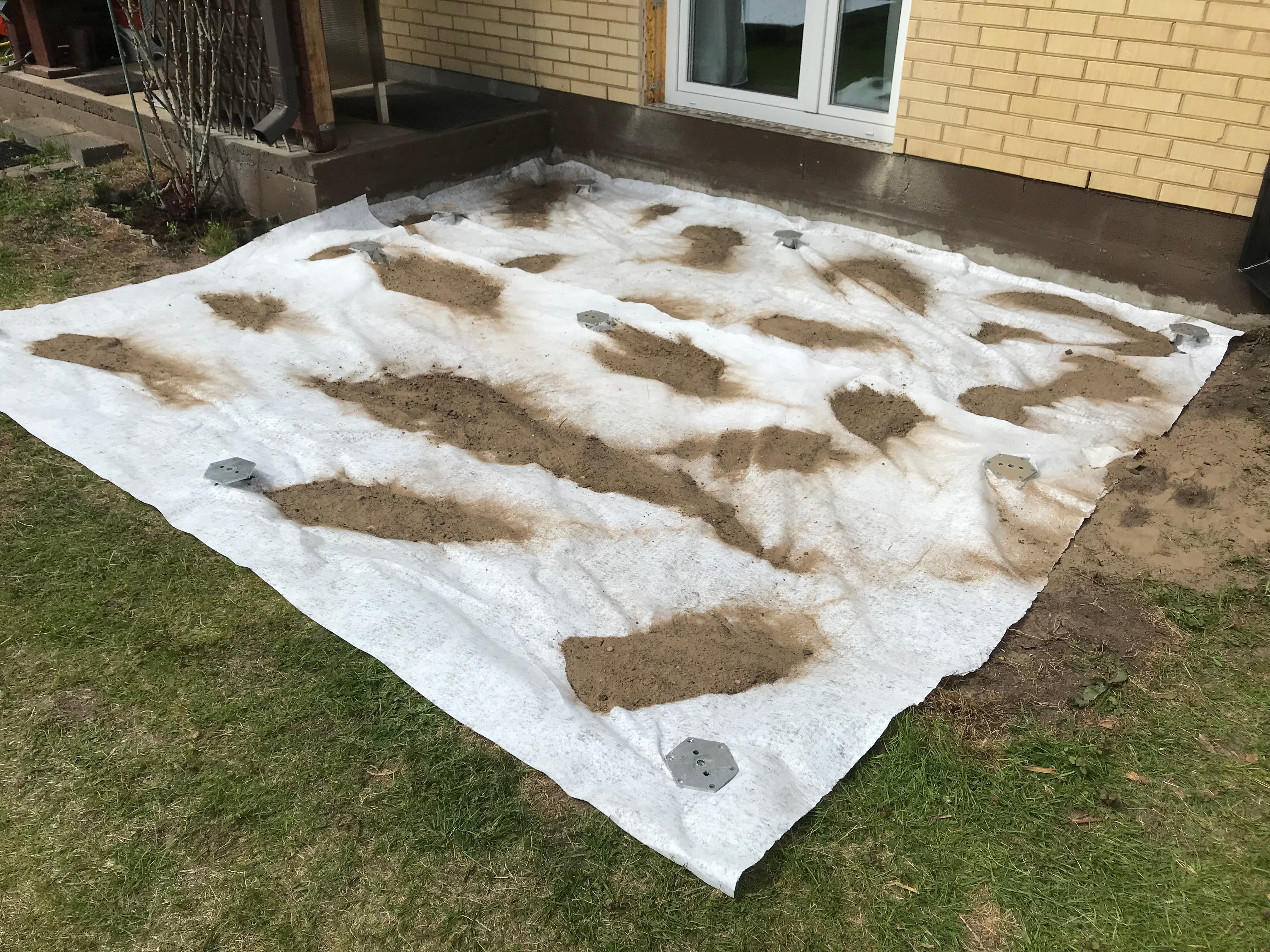 Sheet of white protective plastic with brown patches on a grassy area outside a building.