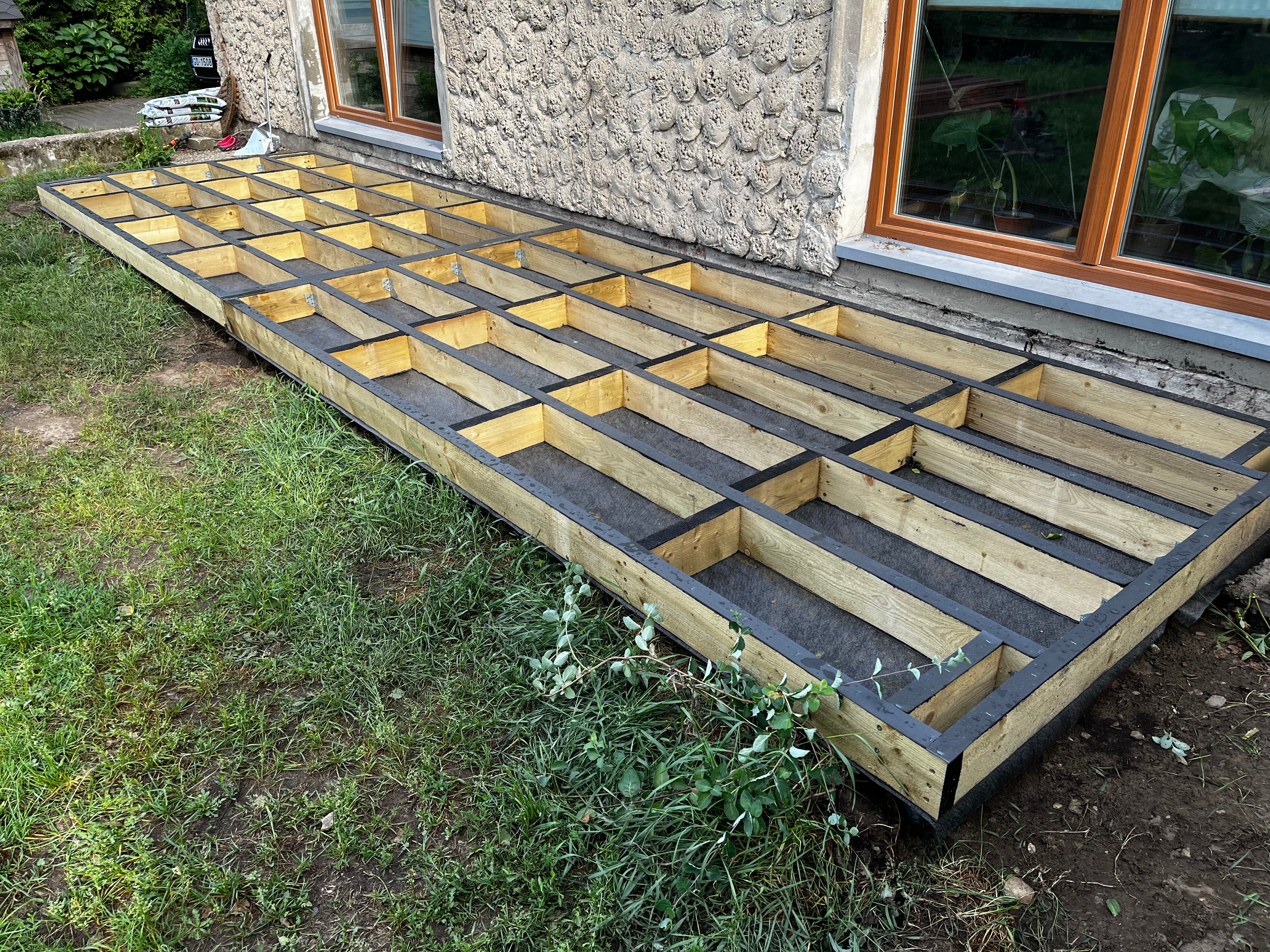 Wooden deck foundation being built against a stone wall.