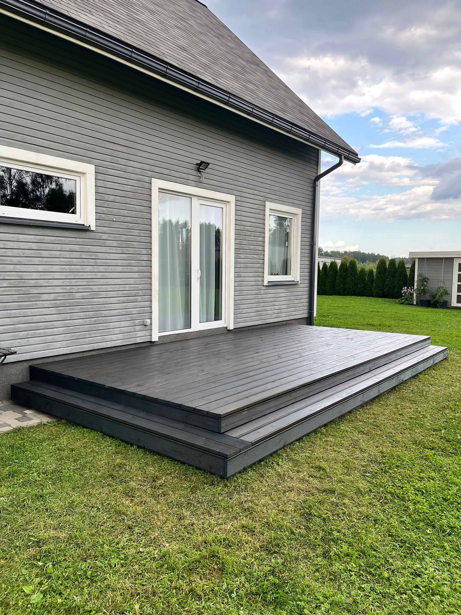 House exterior with gray siding and white windows on a grassy lawn.