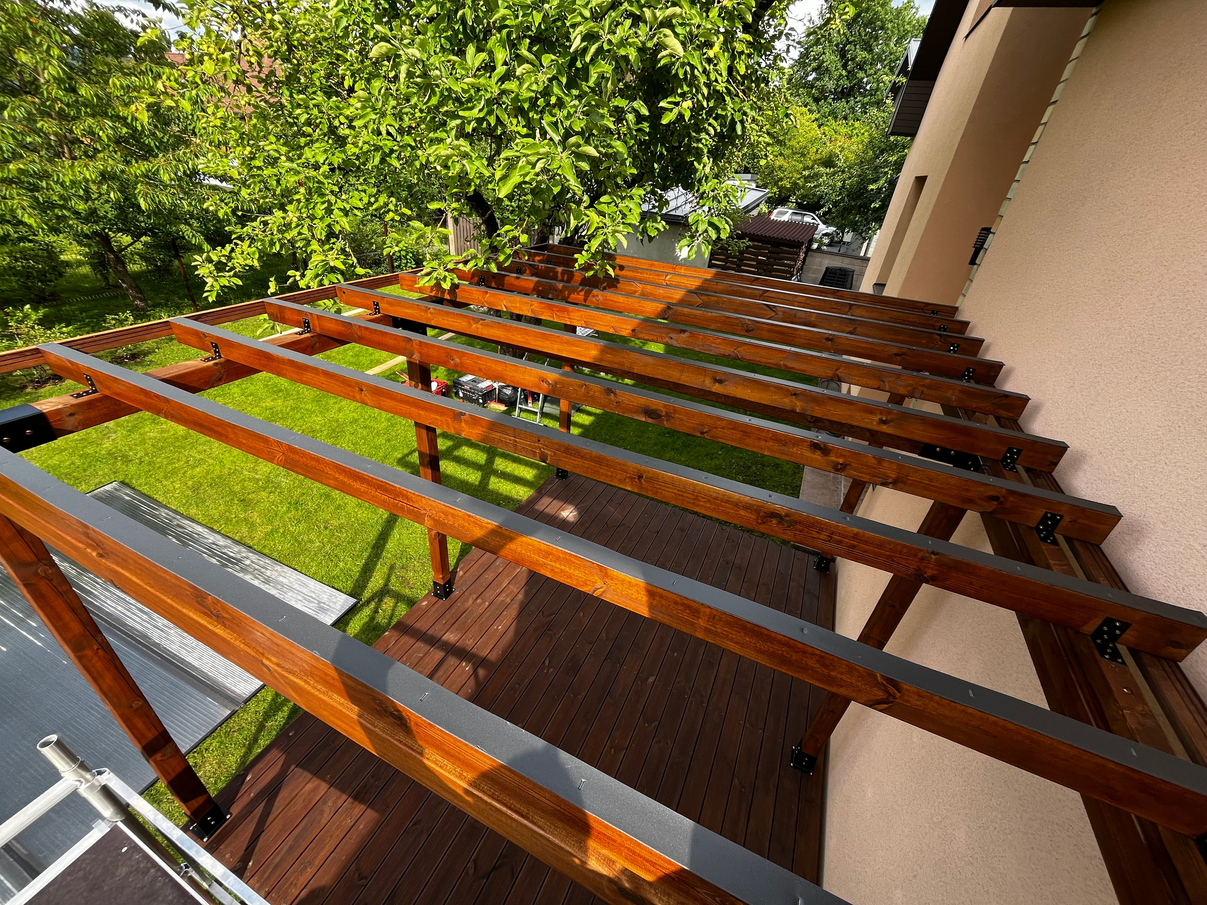 Wooden pergola structure against a building with greenery in the background