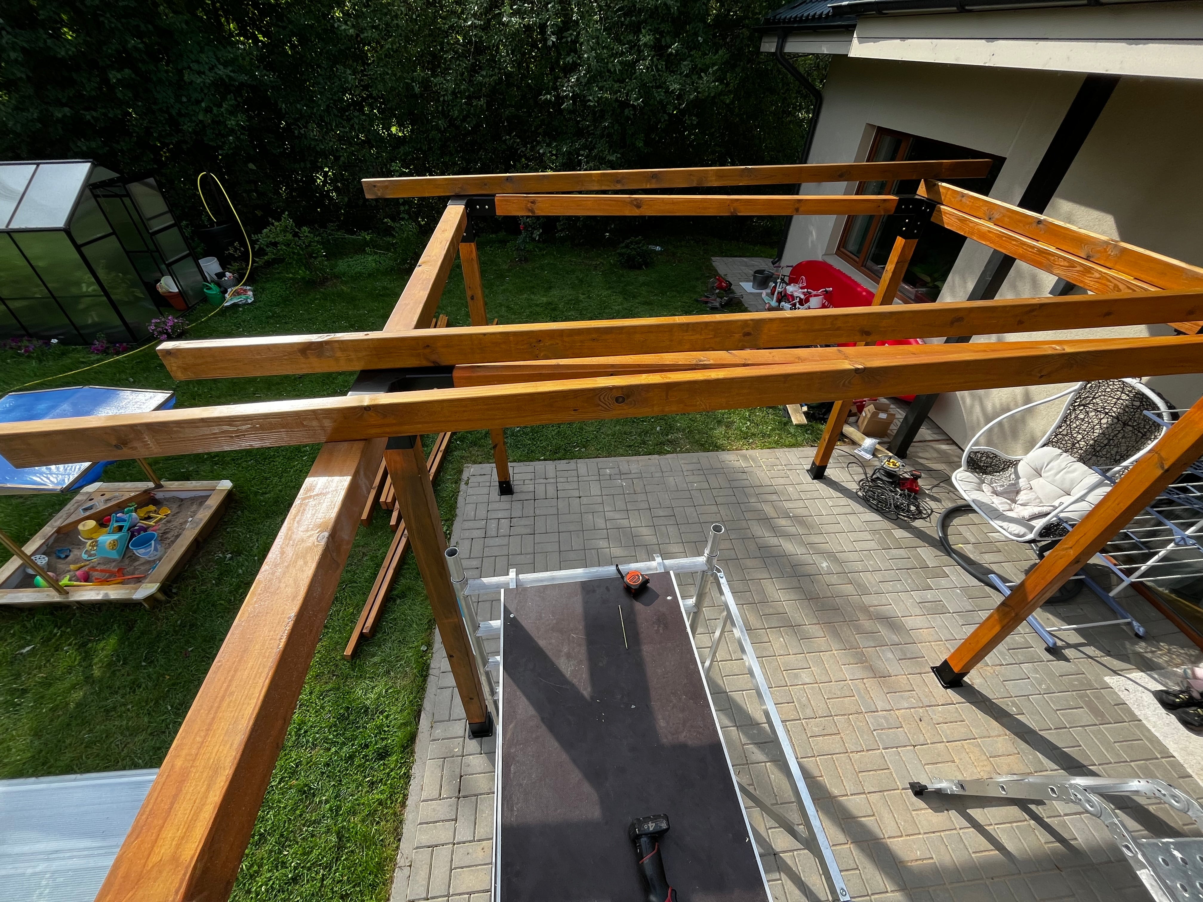Wooden beams on a patio with a pool and garden furniture in the background
