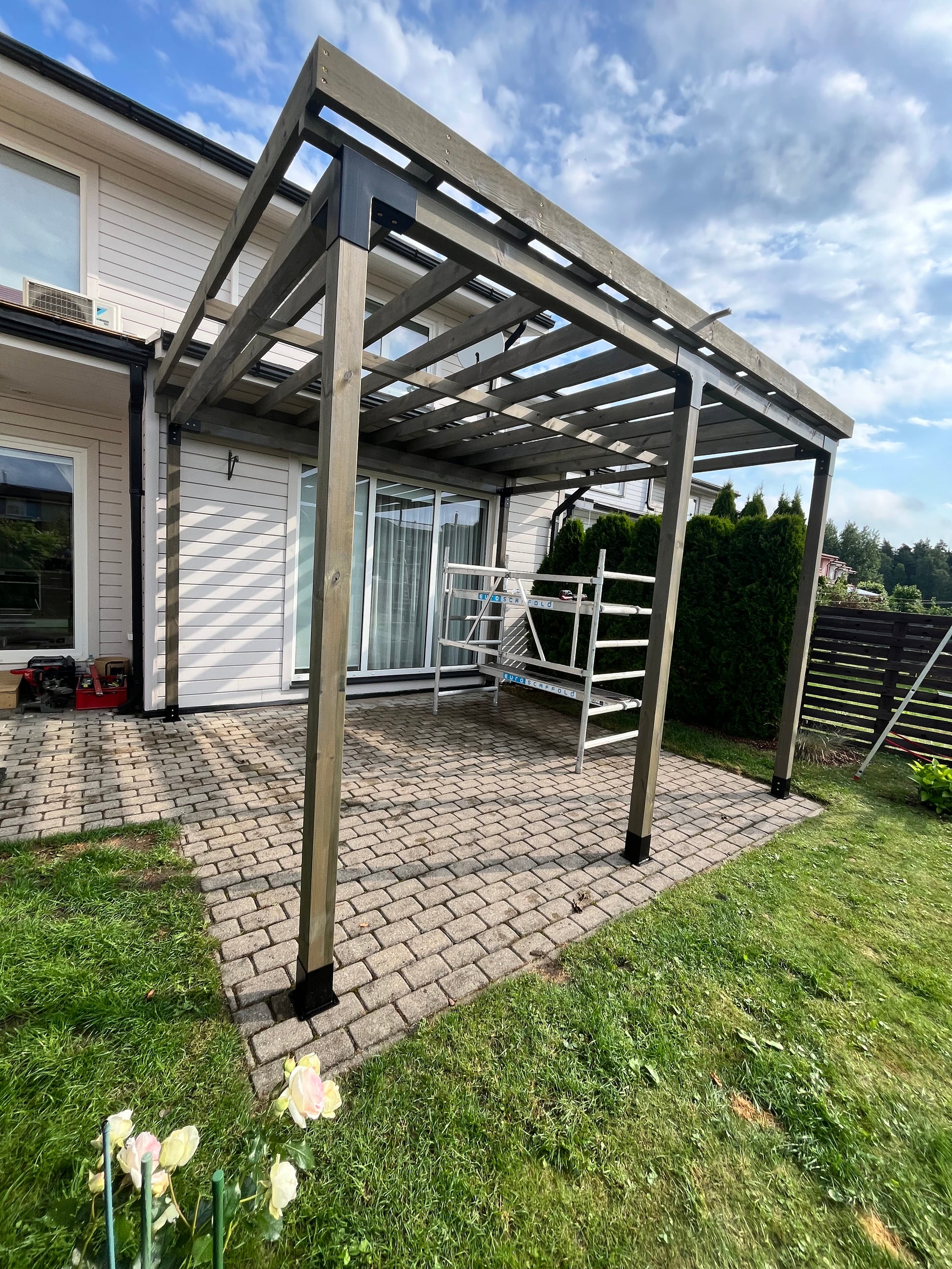 Patio cover attached to a house with grass and flowers in the background