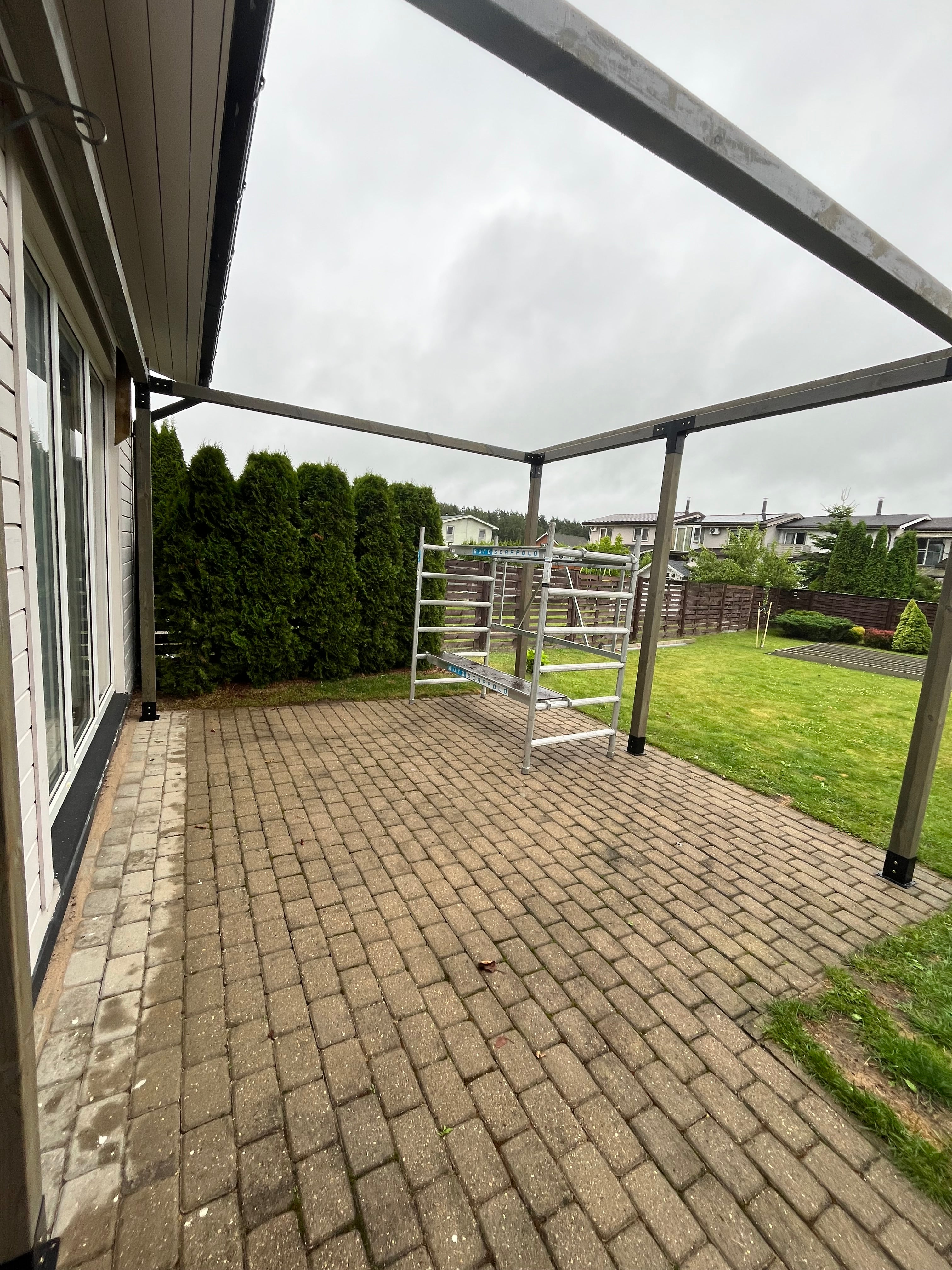 Outdoor patio area with a glass-enclosed pergola on a cloudy day.