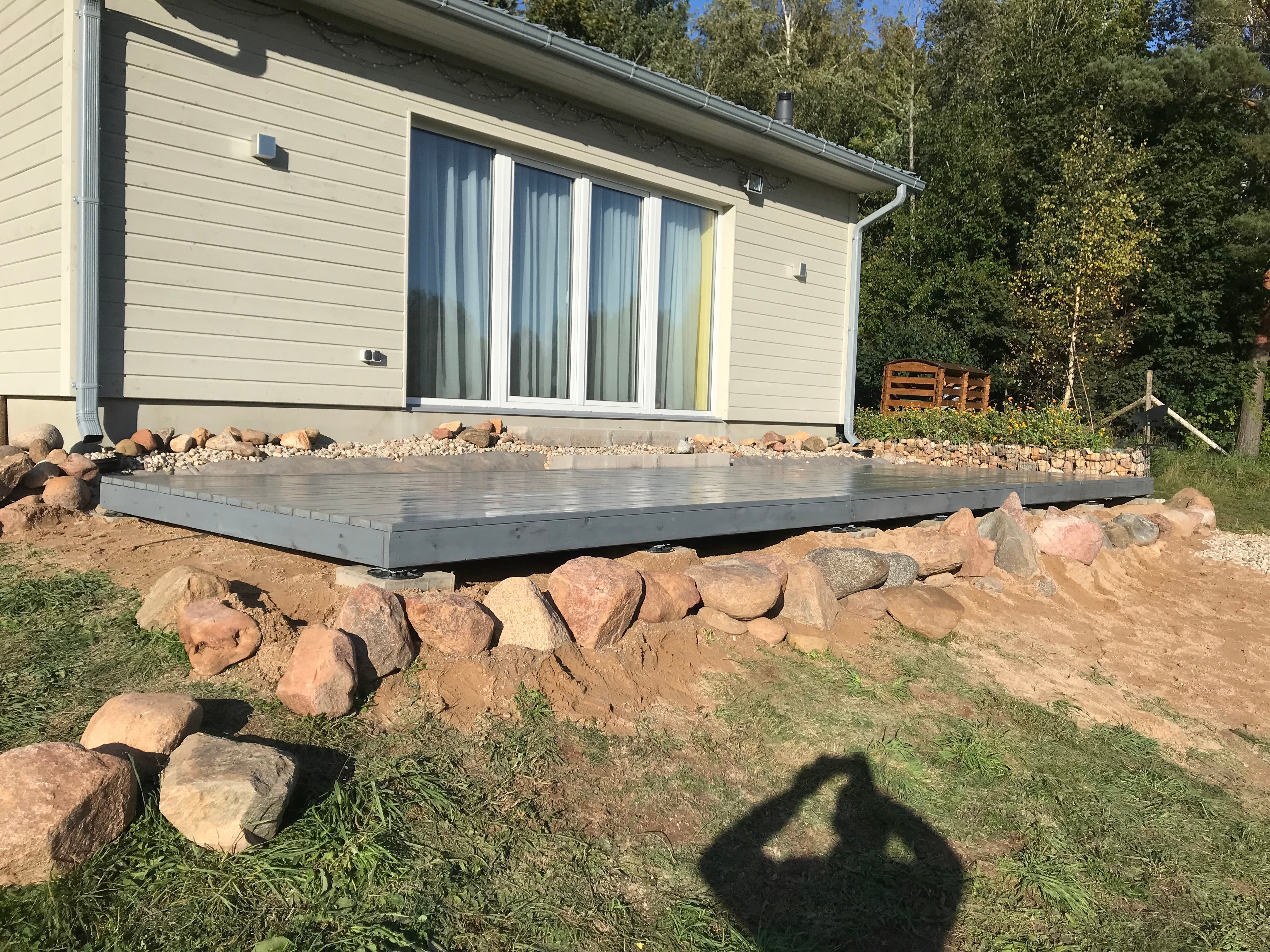 Small house with a newly built wooden deck surrounded by rocks and grass
