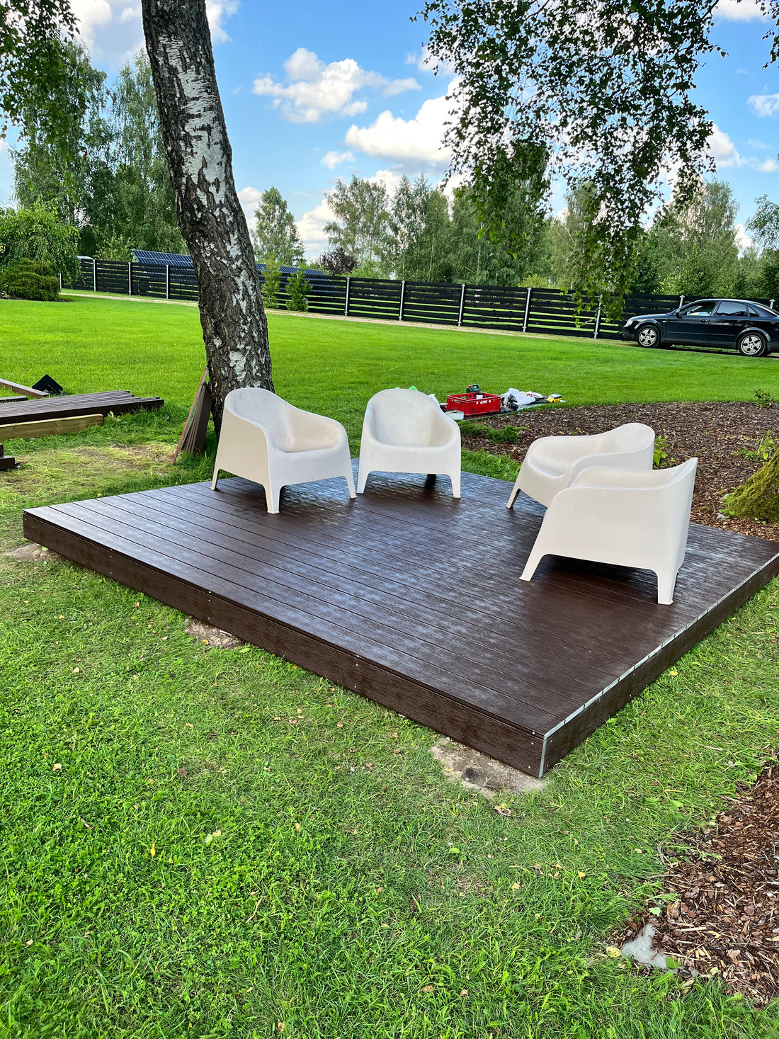 Wooden outdoor deck with chairs on a grassy area with trees in the background