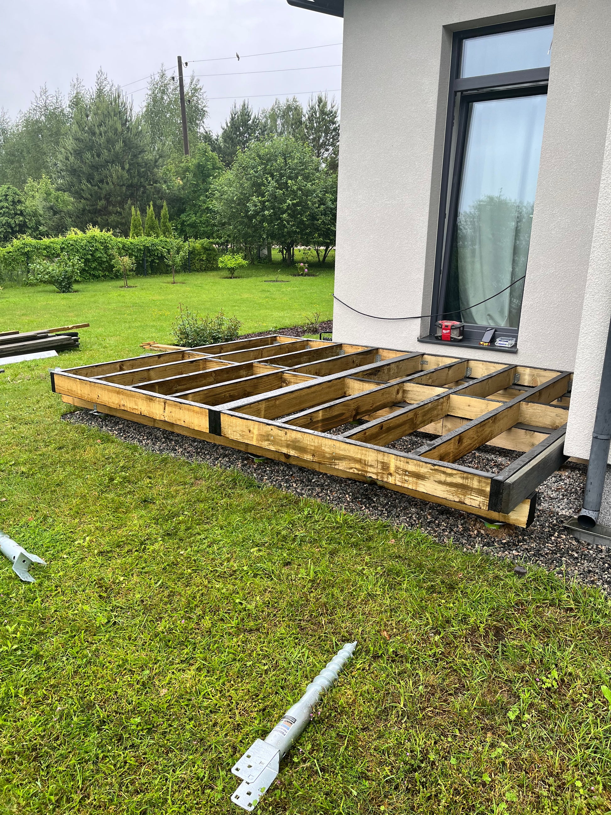 Wooden deck structure next to a house with grass and trees in the background