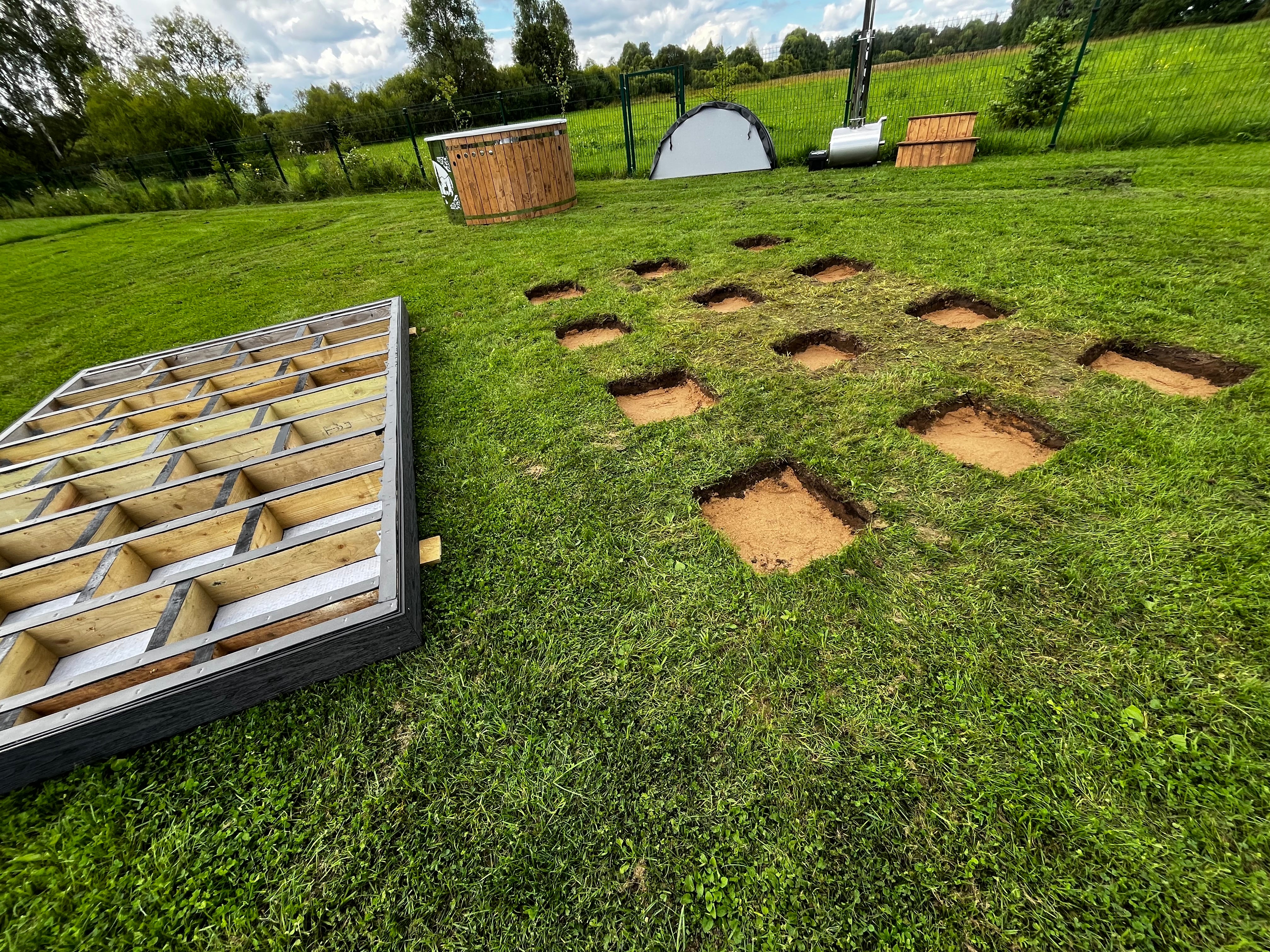 Grid of holes in grass with a metal frame containing more holes in the foreground