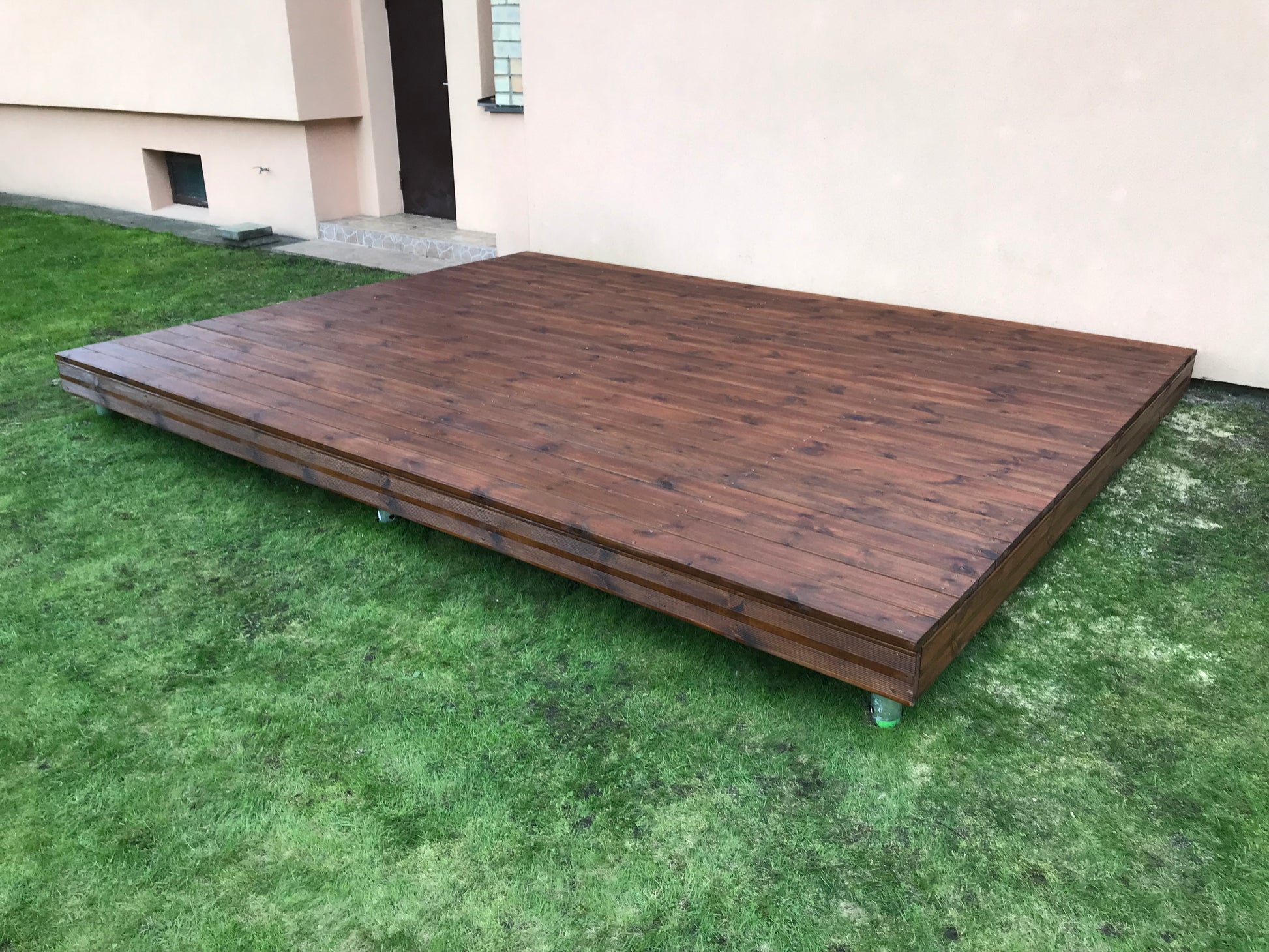 Wooden deck on grass with a building in the background