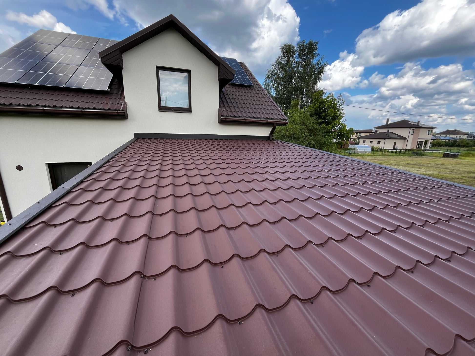 House with a brown roof and solar panels on a partly cloudy day