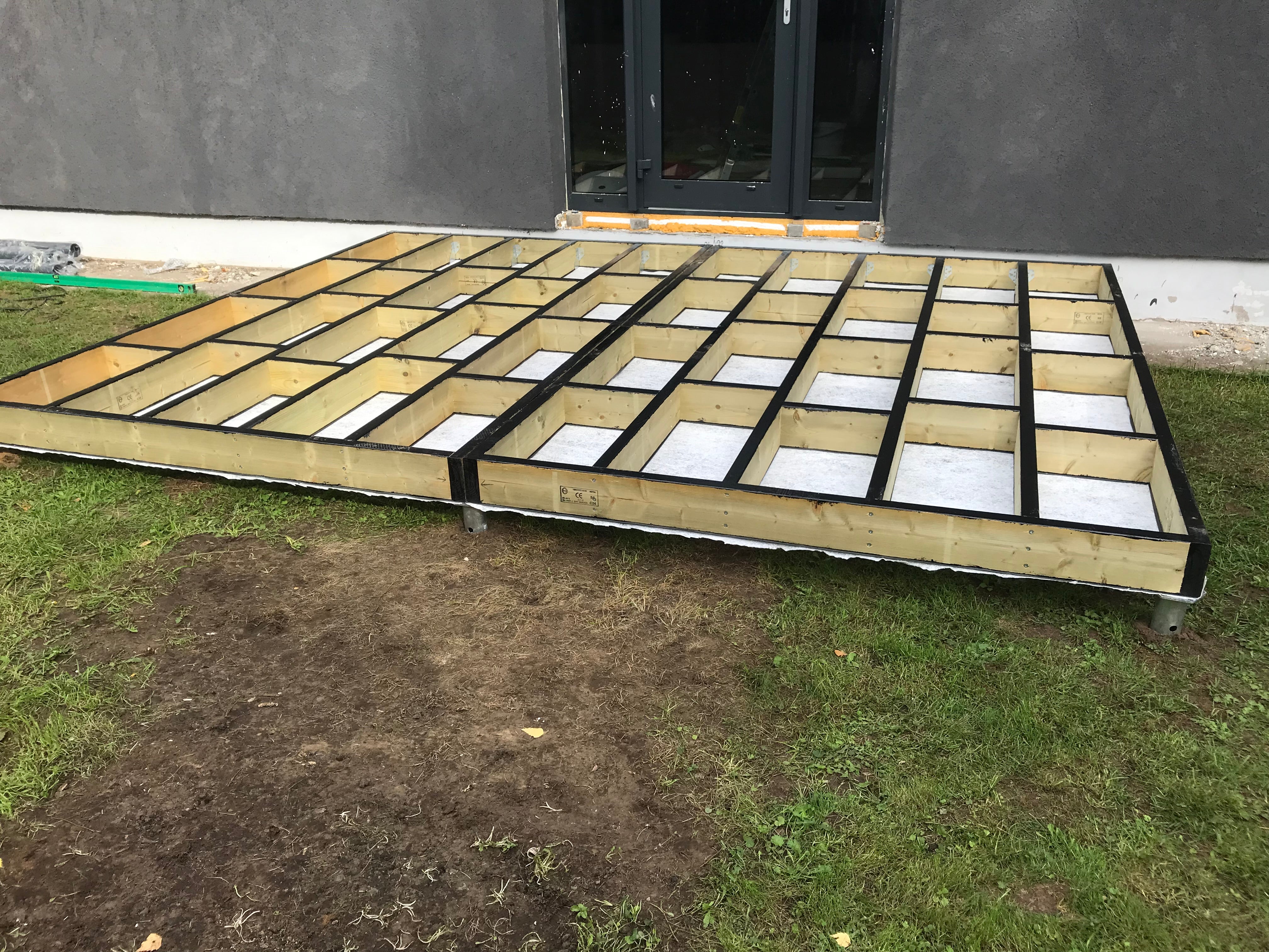 Large wooden platform with grid pattern on grass, possibly for construction or storage.