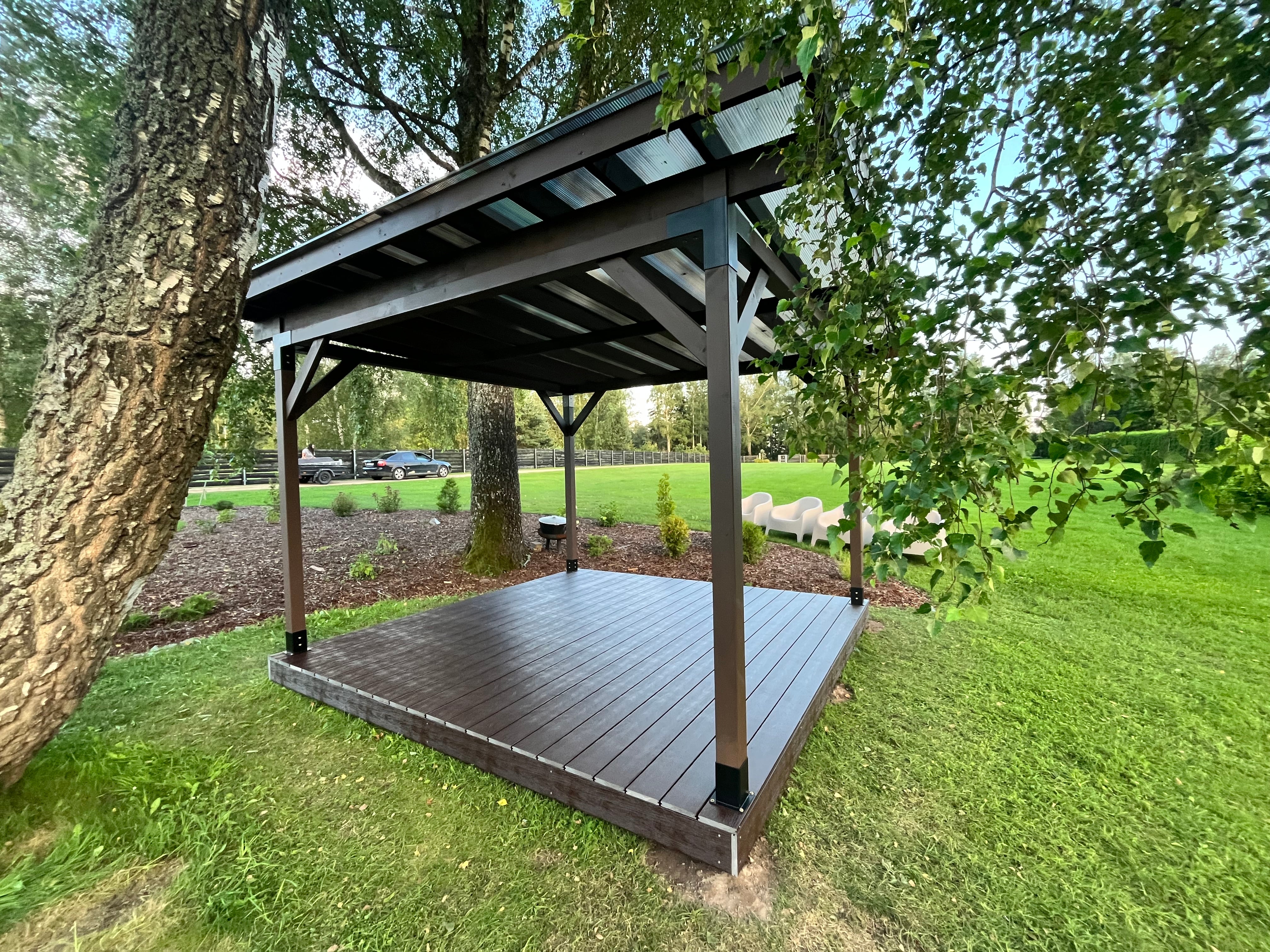 Wooden pergola structure in a garden setting with grass and trees.