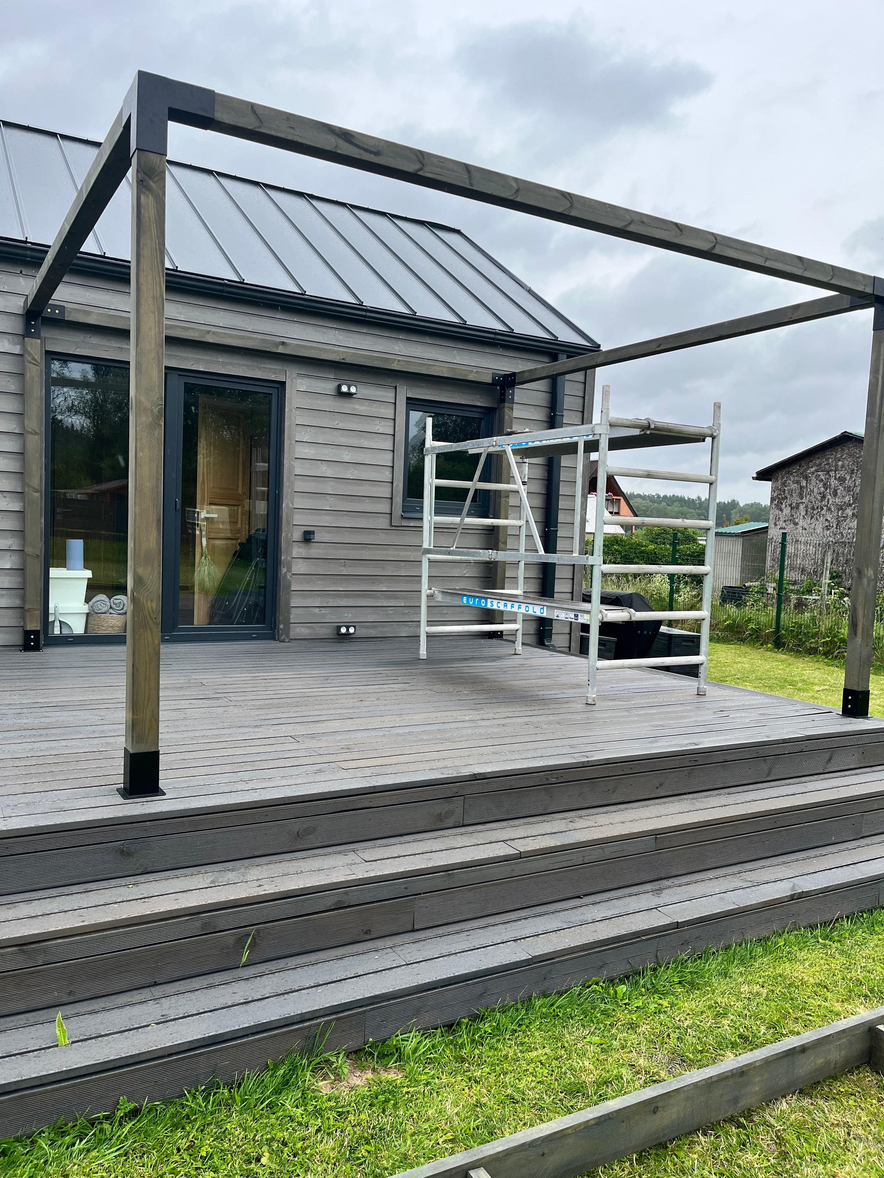 A modern house with a glass wall and metal frame, surrounded by grass and a cloudy sky.