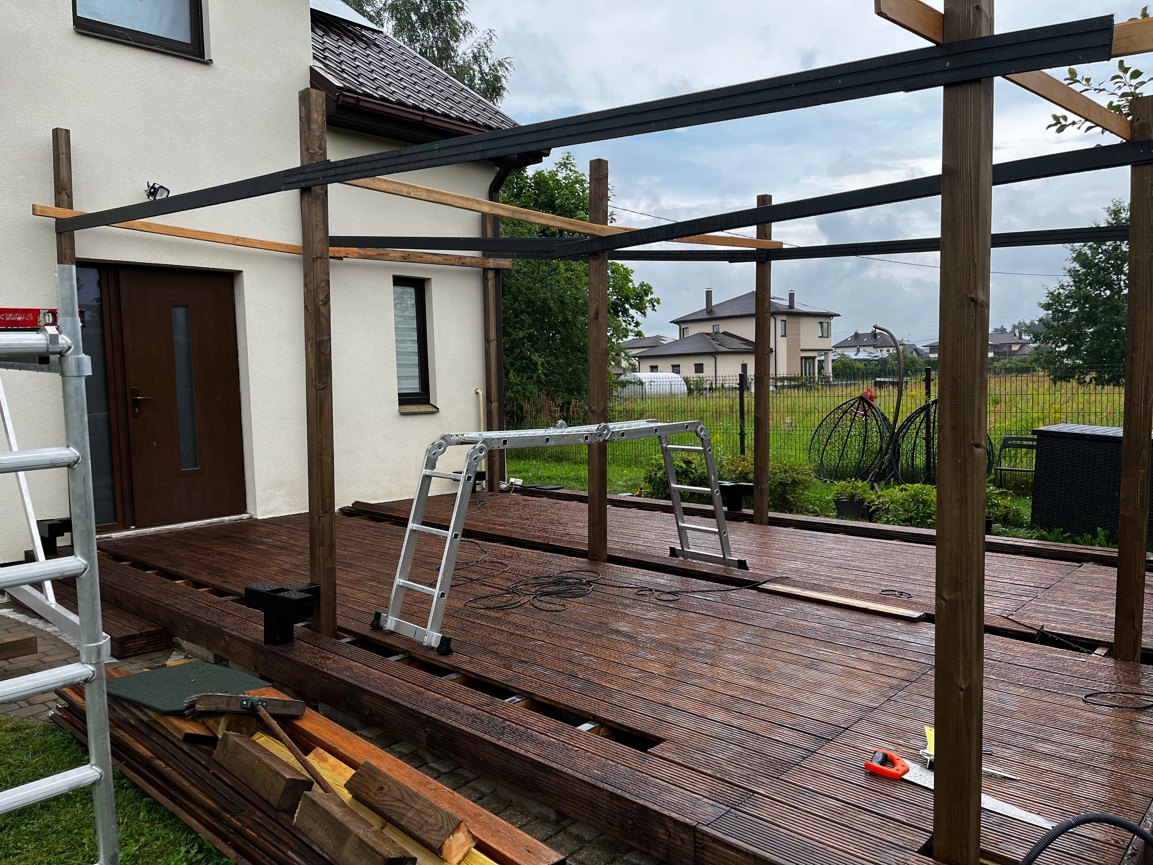 Wooden deck under construction with scaffolding and tools in a residential area.