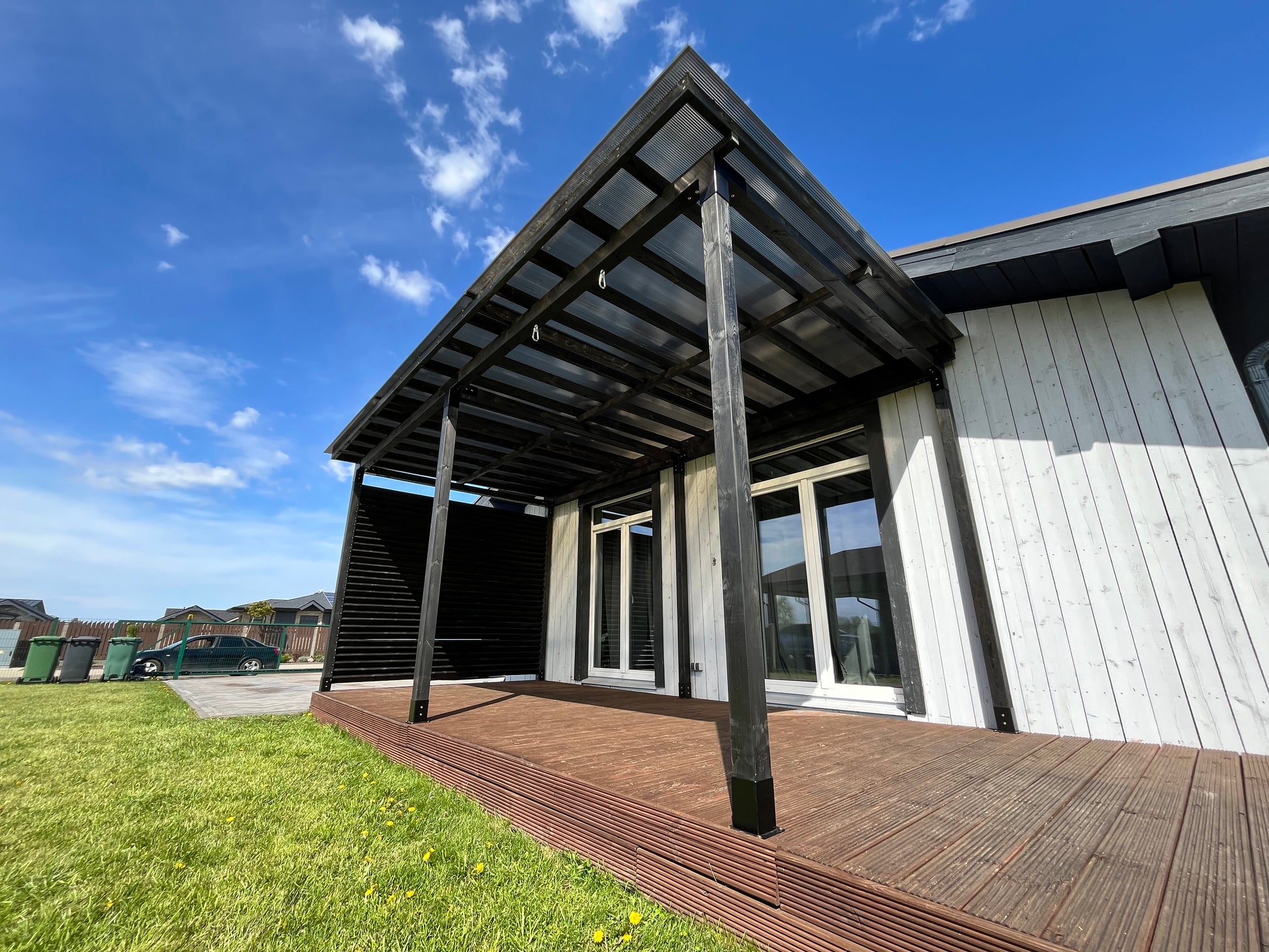 Modern house exterior with a wooden deck and grassy area under a blue sky.