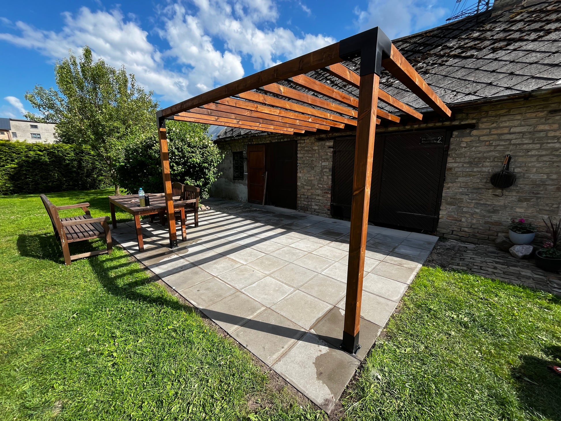 Patio area with wooden pergola, table, and chairs on a sunny day.