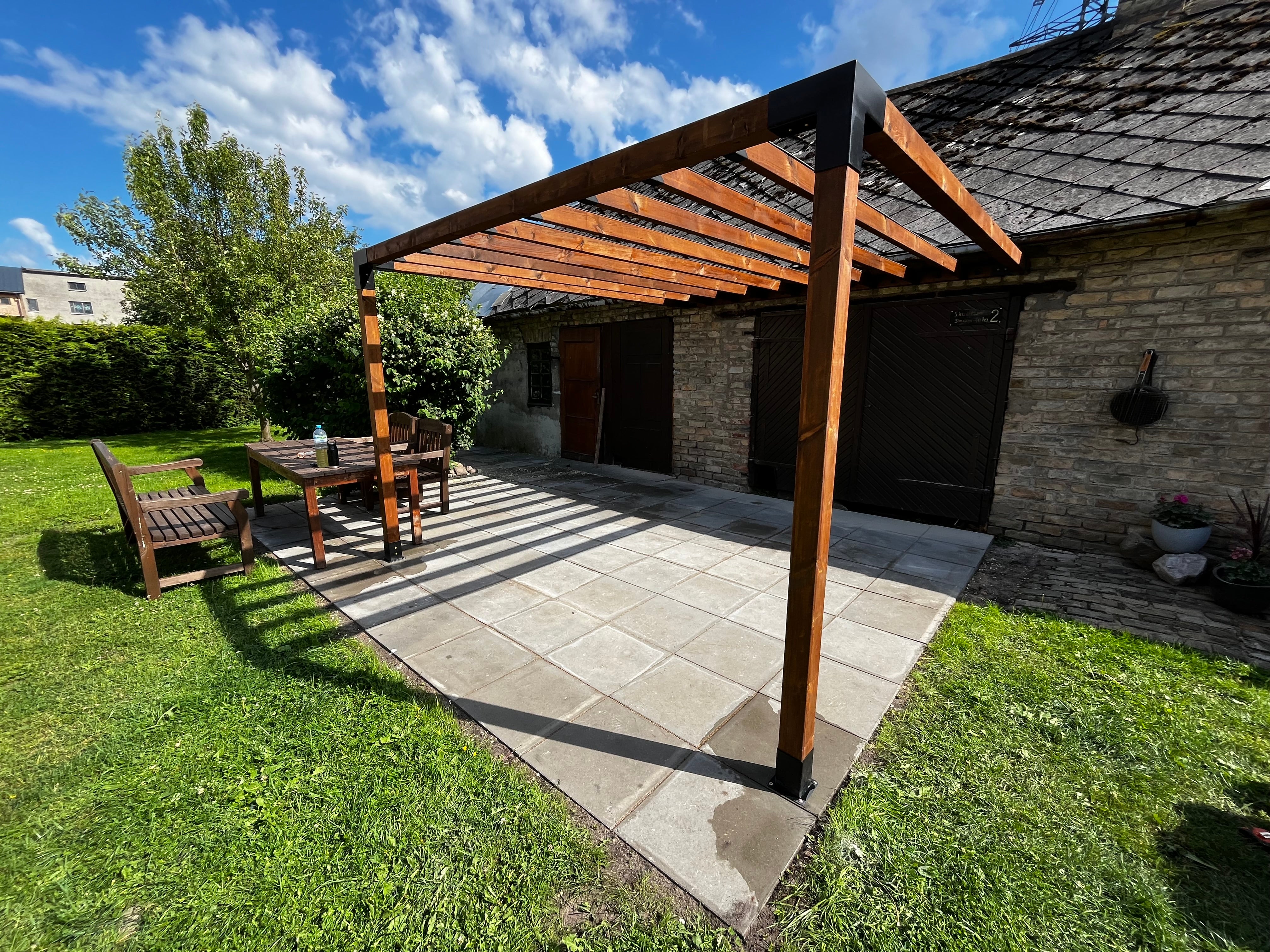 Patio area with wooden pergola, table, and chairs on a sunny day.