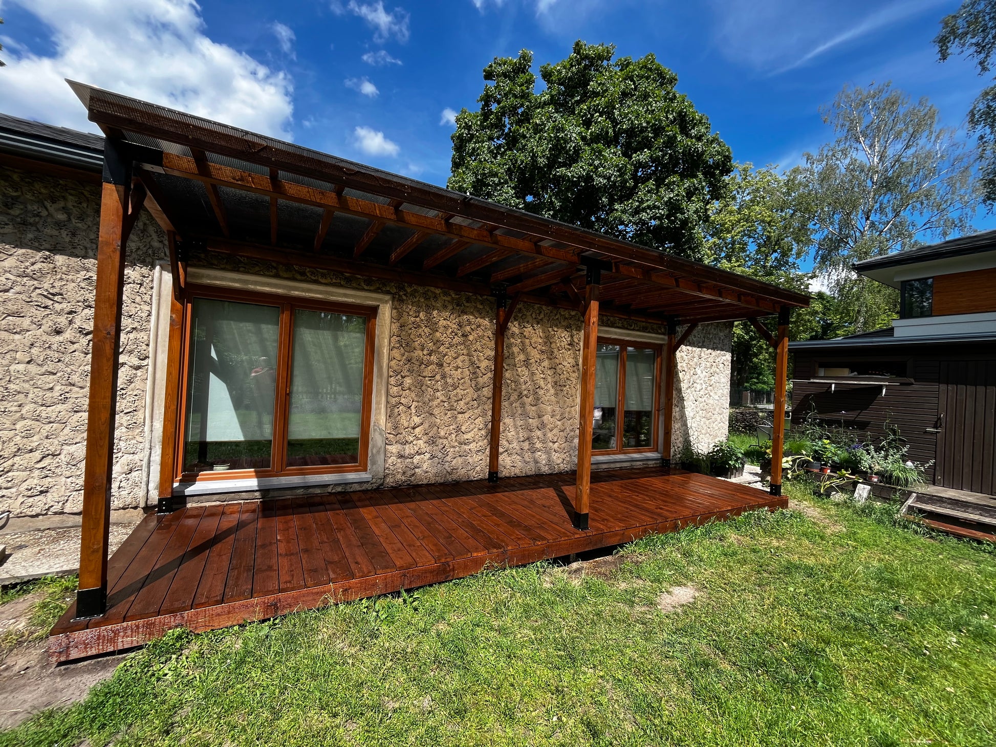 Wooden deck extension on a house with stone walls and a garden area.