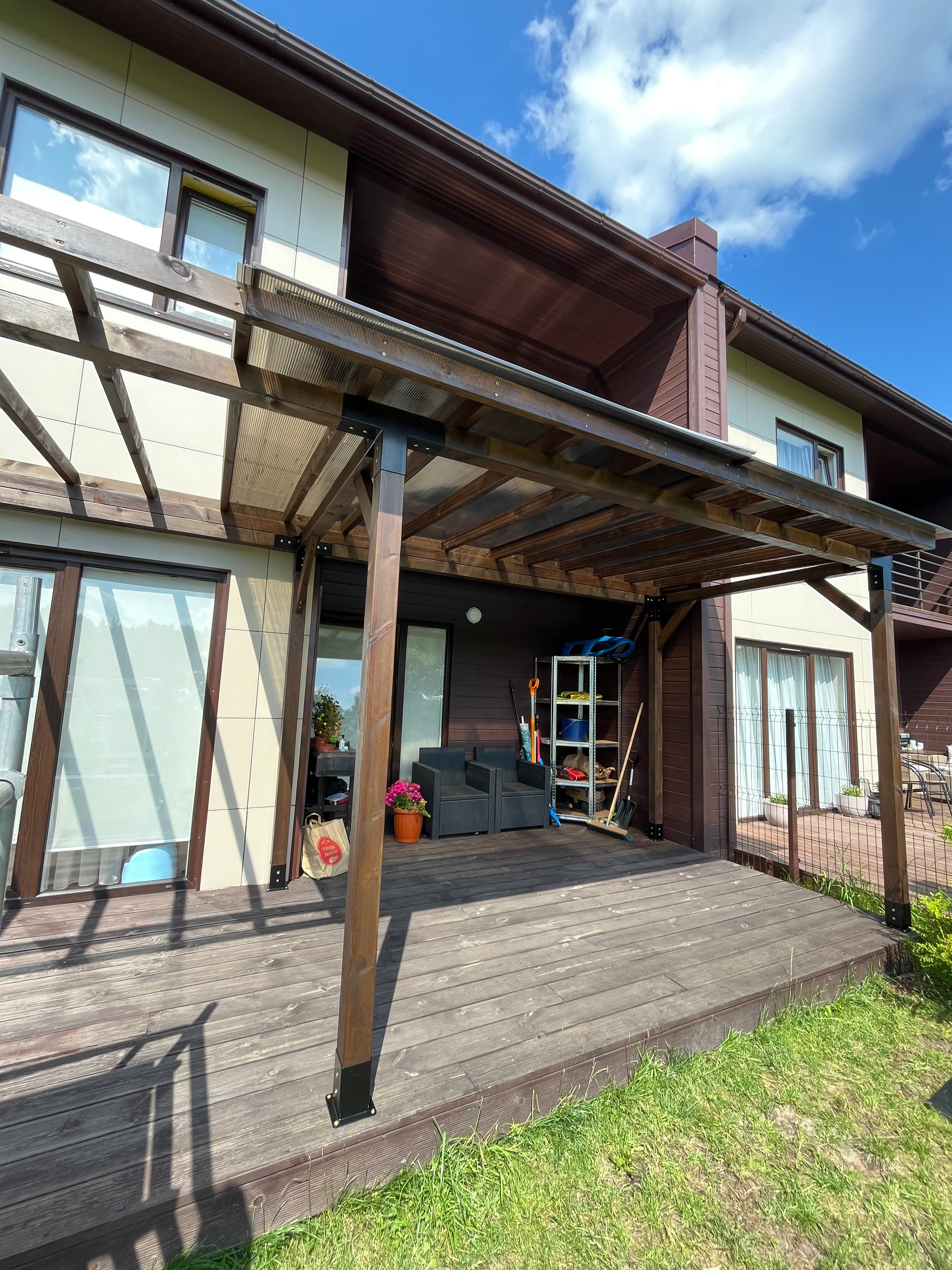 Wooden deck with canopy leading to a house with a blue sky and clouds.
