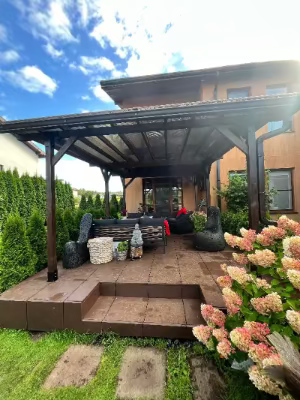 Outdoor patio area with a wooden pergola, furniture, and flowers on a sunny day.