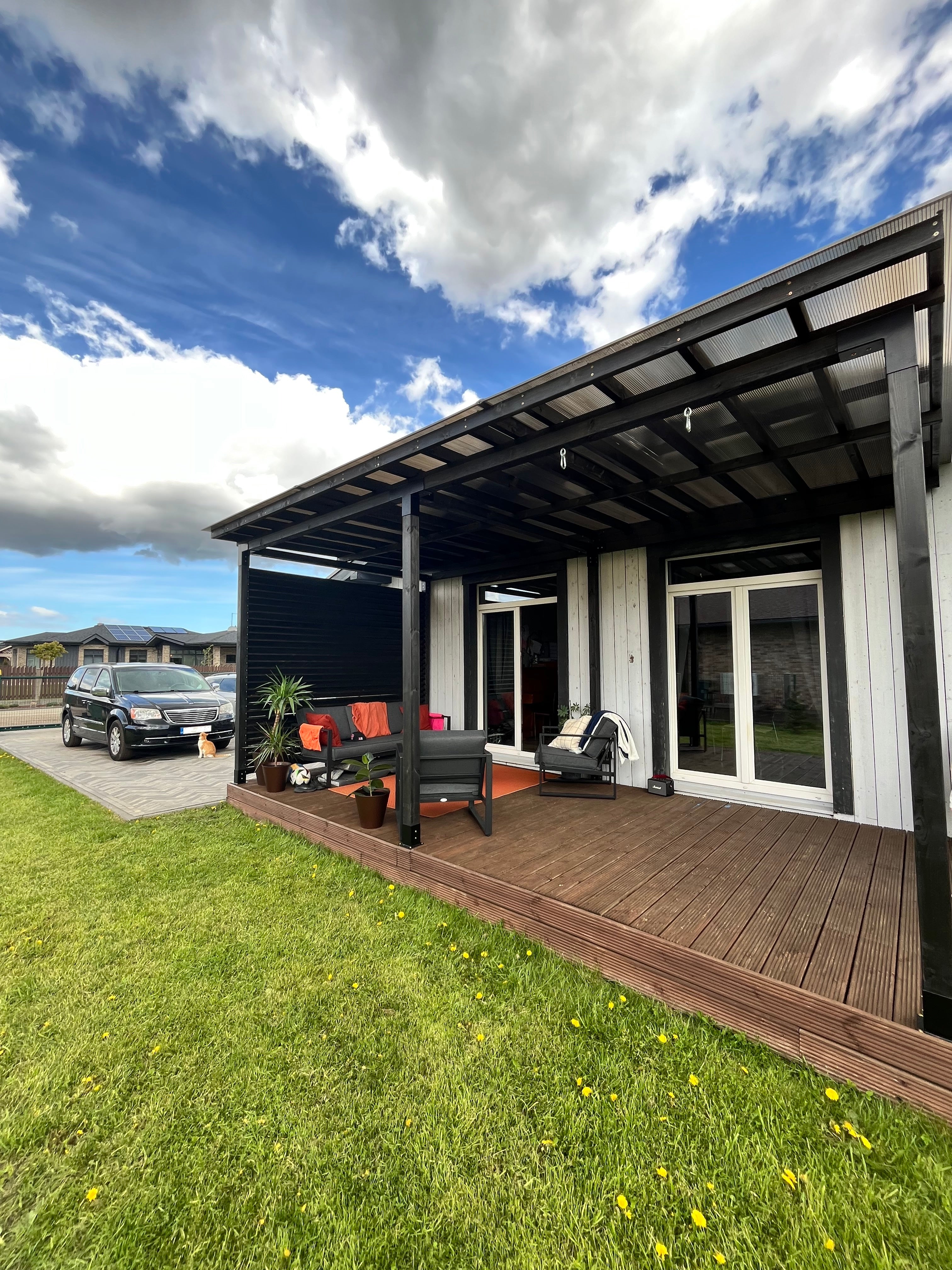 Modern house exterior with a deck, lawn, and car in the driveway under a blue sky.