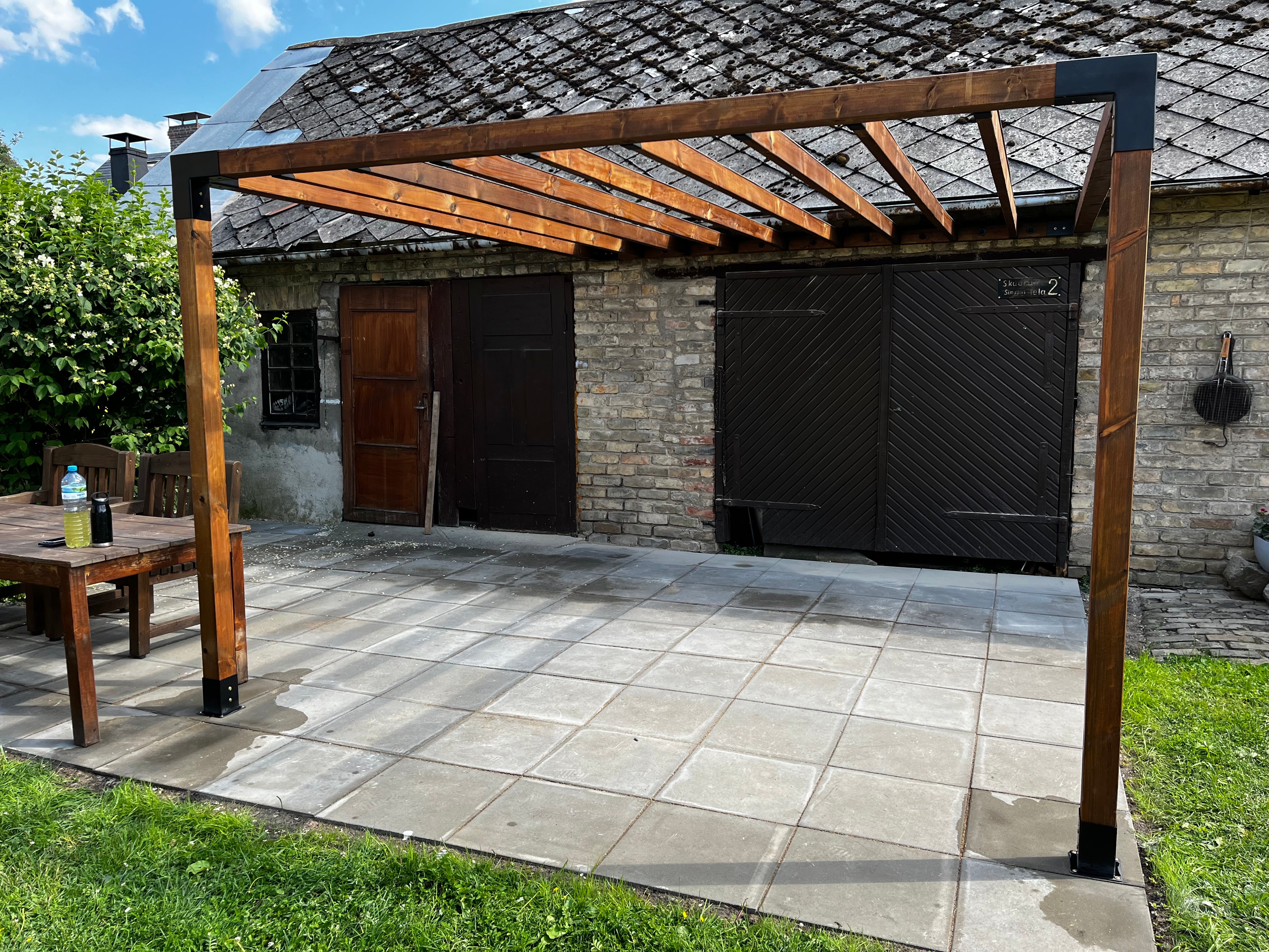 Wooden pergola on a patio area with a stone wall and garden furniture in the background.