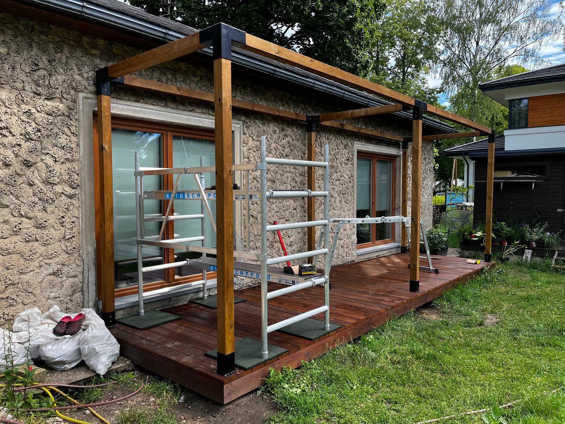 Outdoor area with a wooden deck and metal ladders against a stone wall.