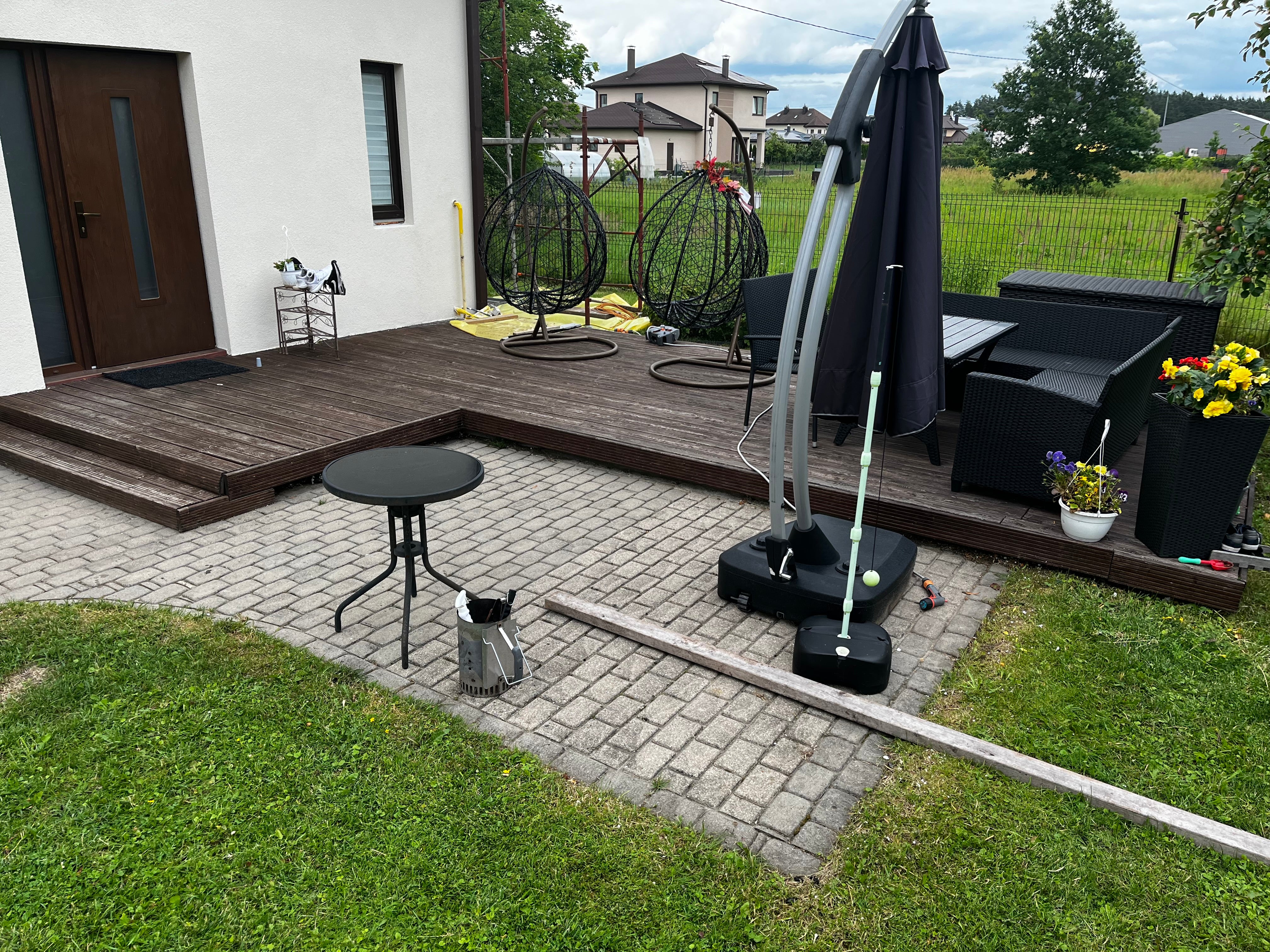 Backyard with patio furniture, umbrella, and garden tools on a paved area.