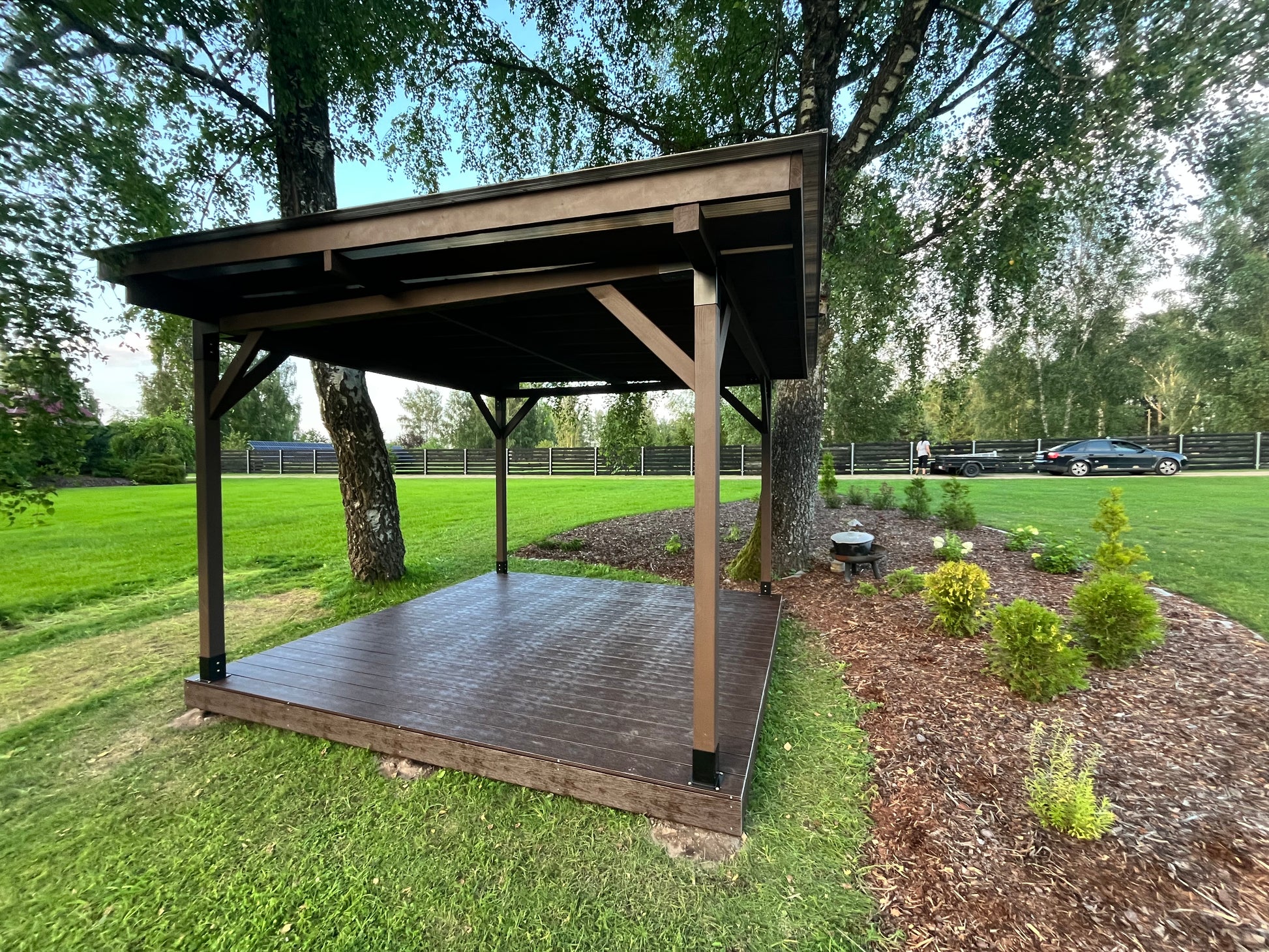 Wooden gazebo in a park setting with trees and grass.