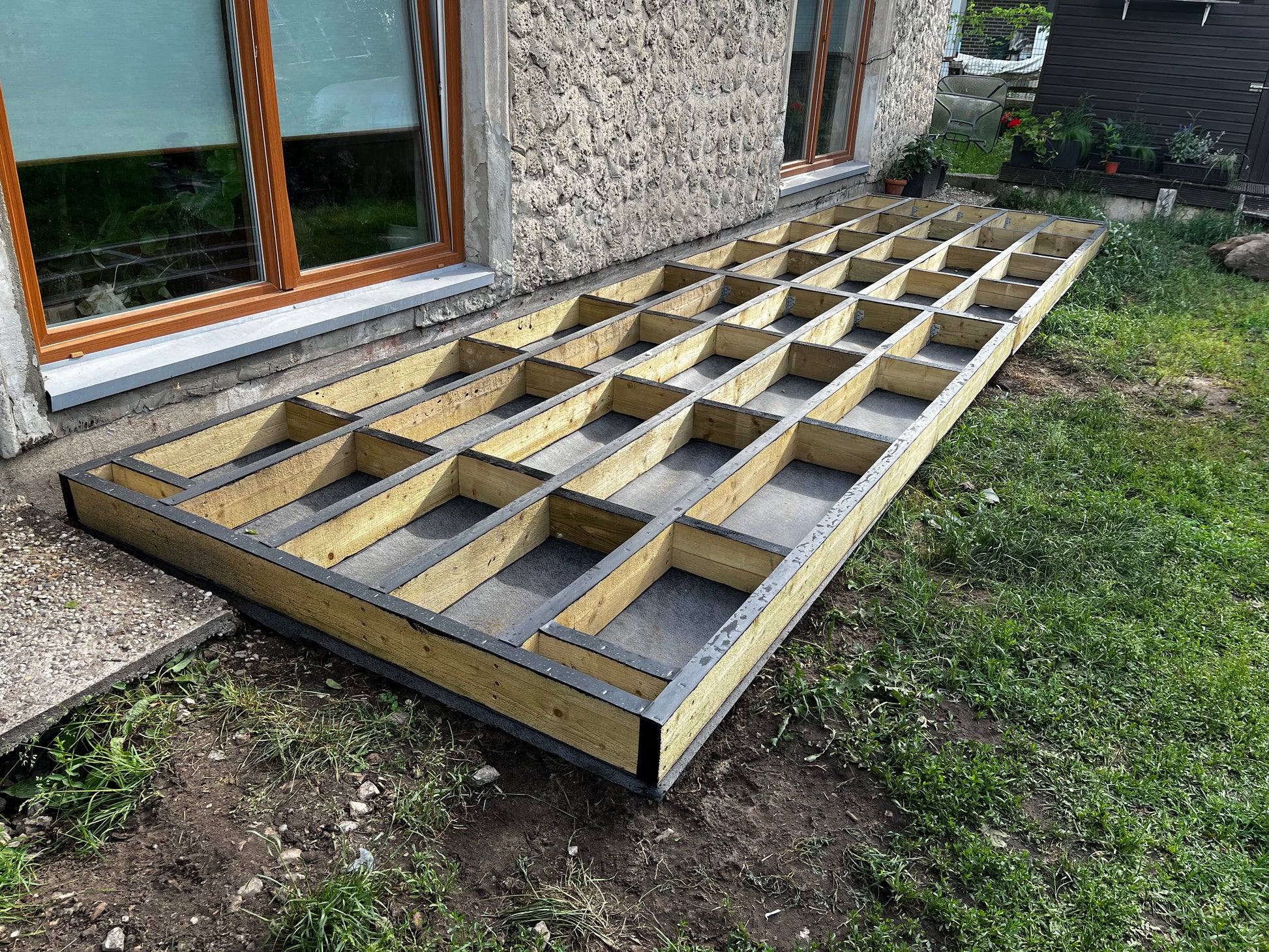 Wooden deck floor joists on the ground in front of a house