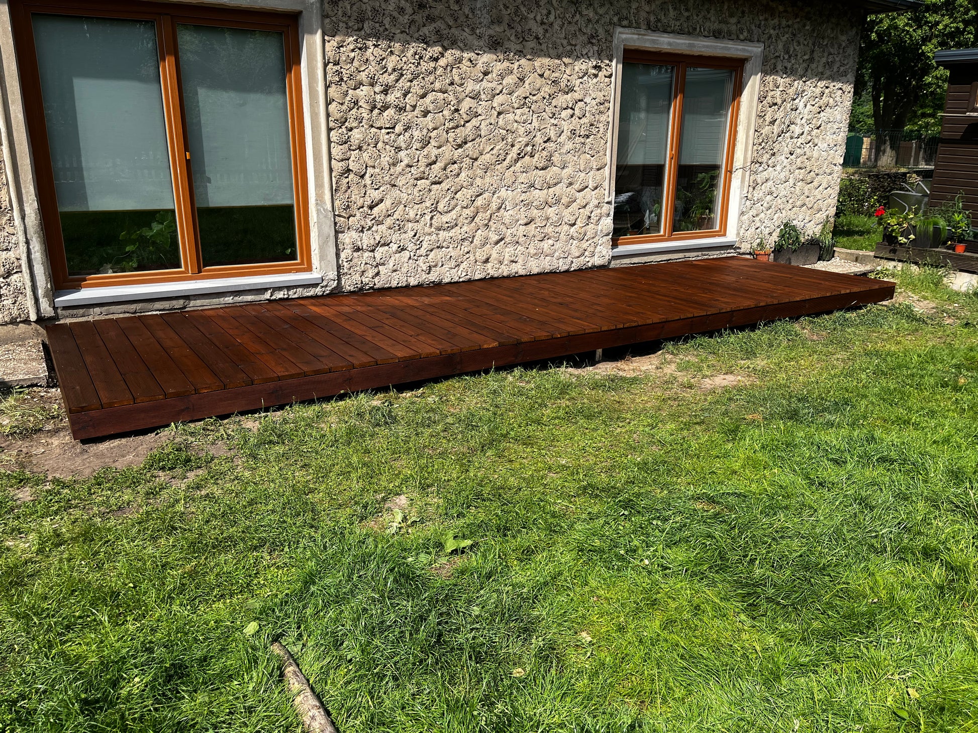 Wooden deck extending from a stone house with large windows.