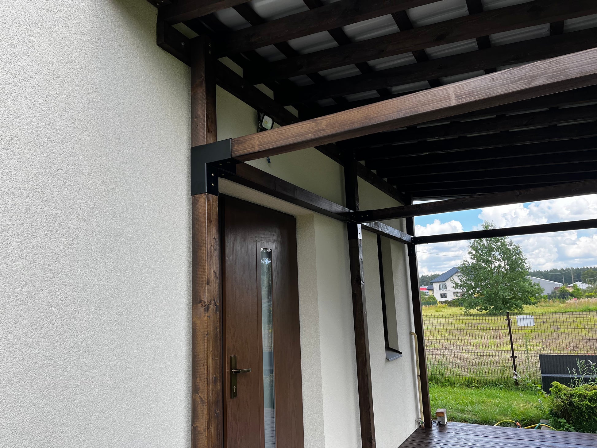 Wooden pergola attached to a house with a view of a field and trees.