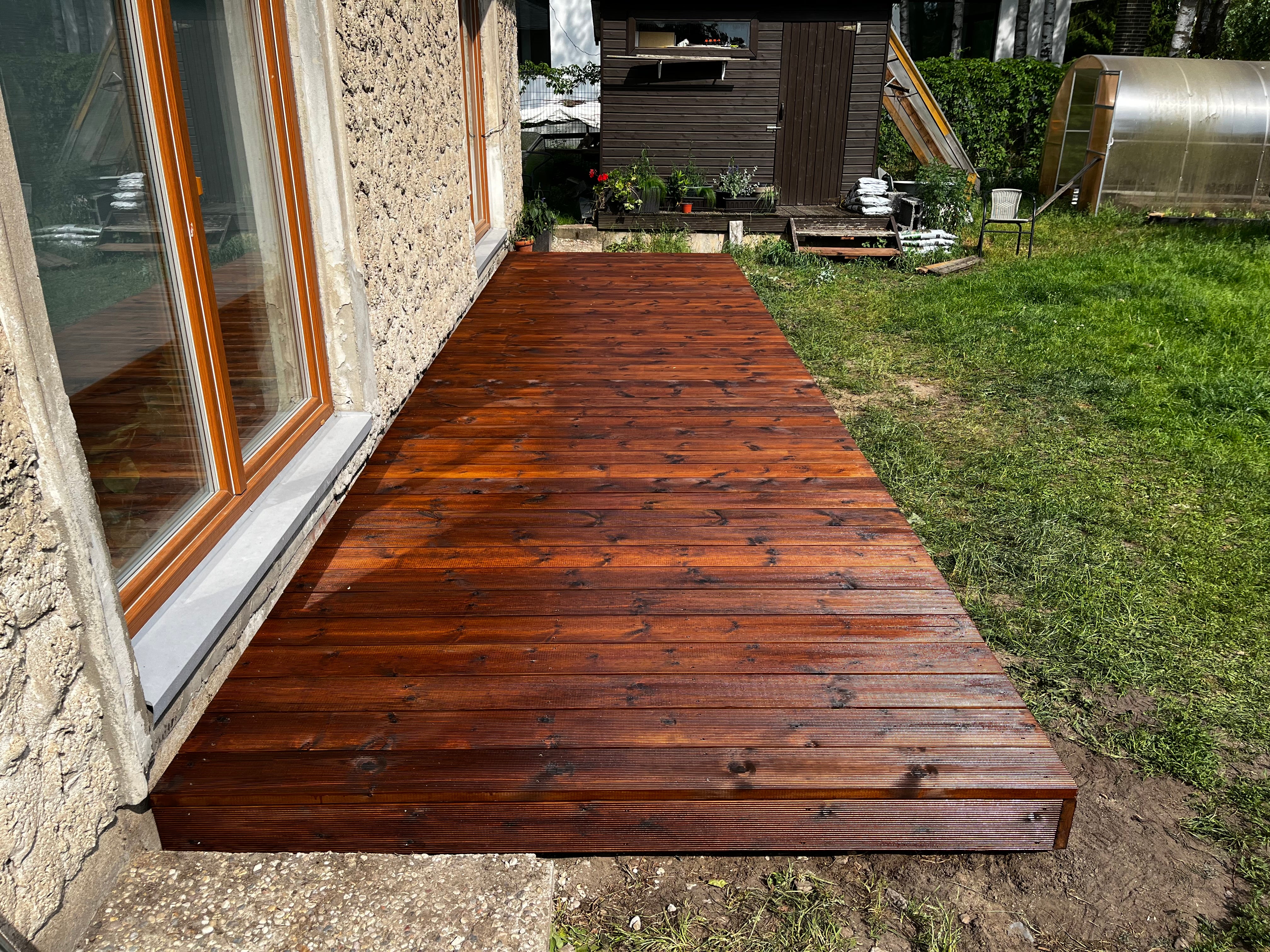 Wooden deck extending from a building with a grassy area and garden in the background