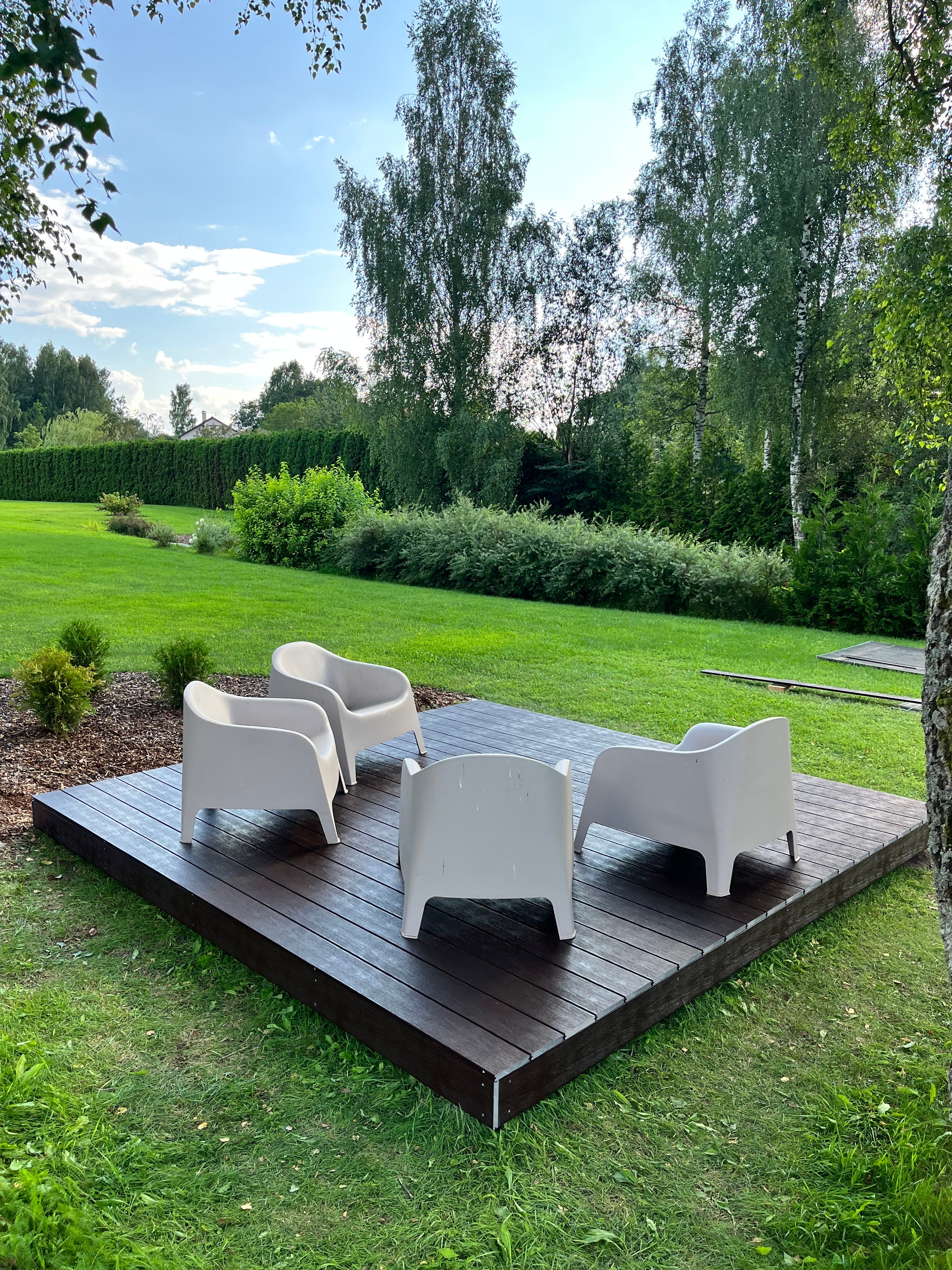 Modern outdoor furniture set on a wooden deck with greenery in the background