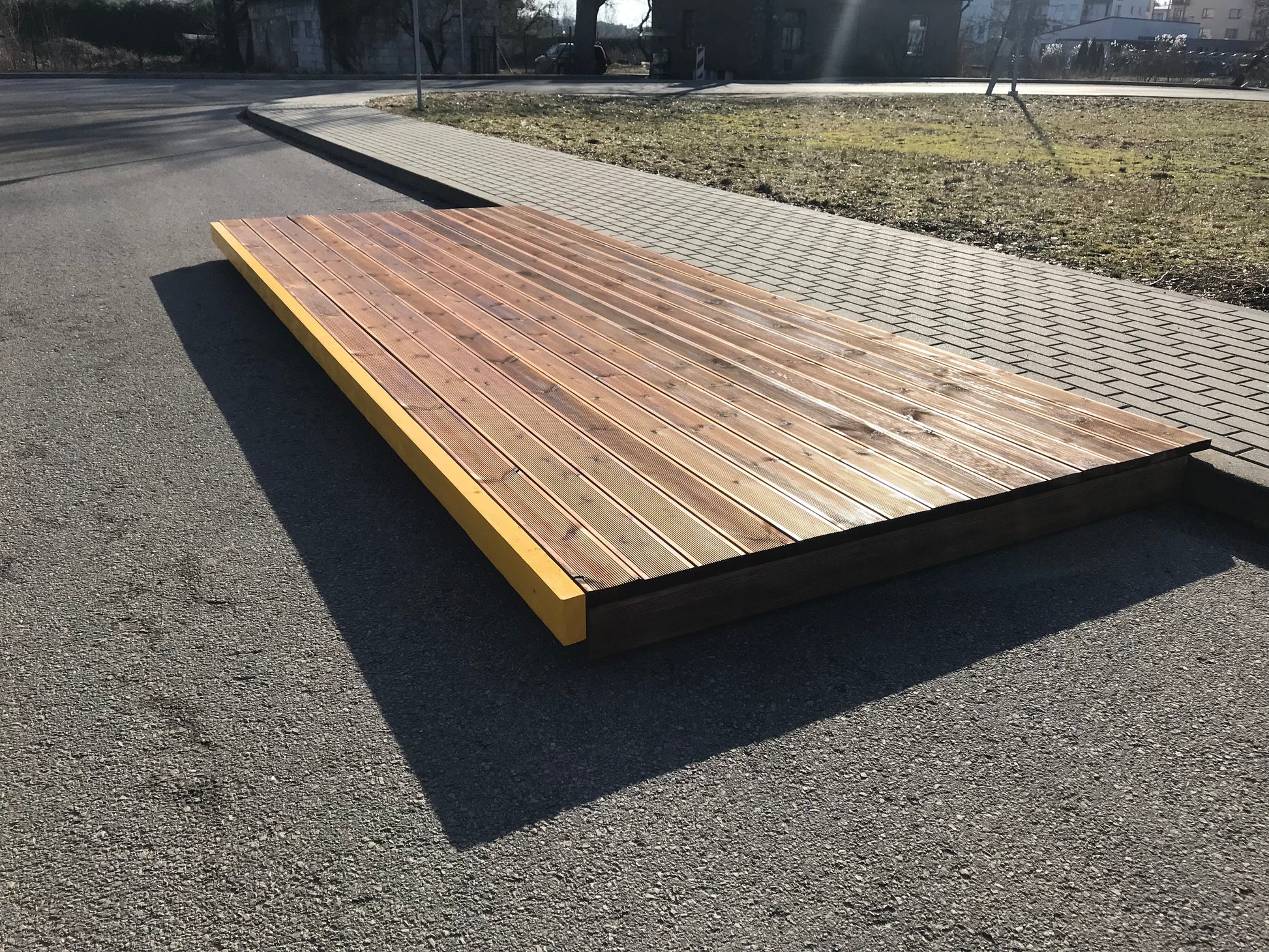 Wooden platform on an asphalt surface with grass and pavement in the background
