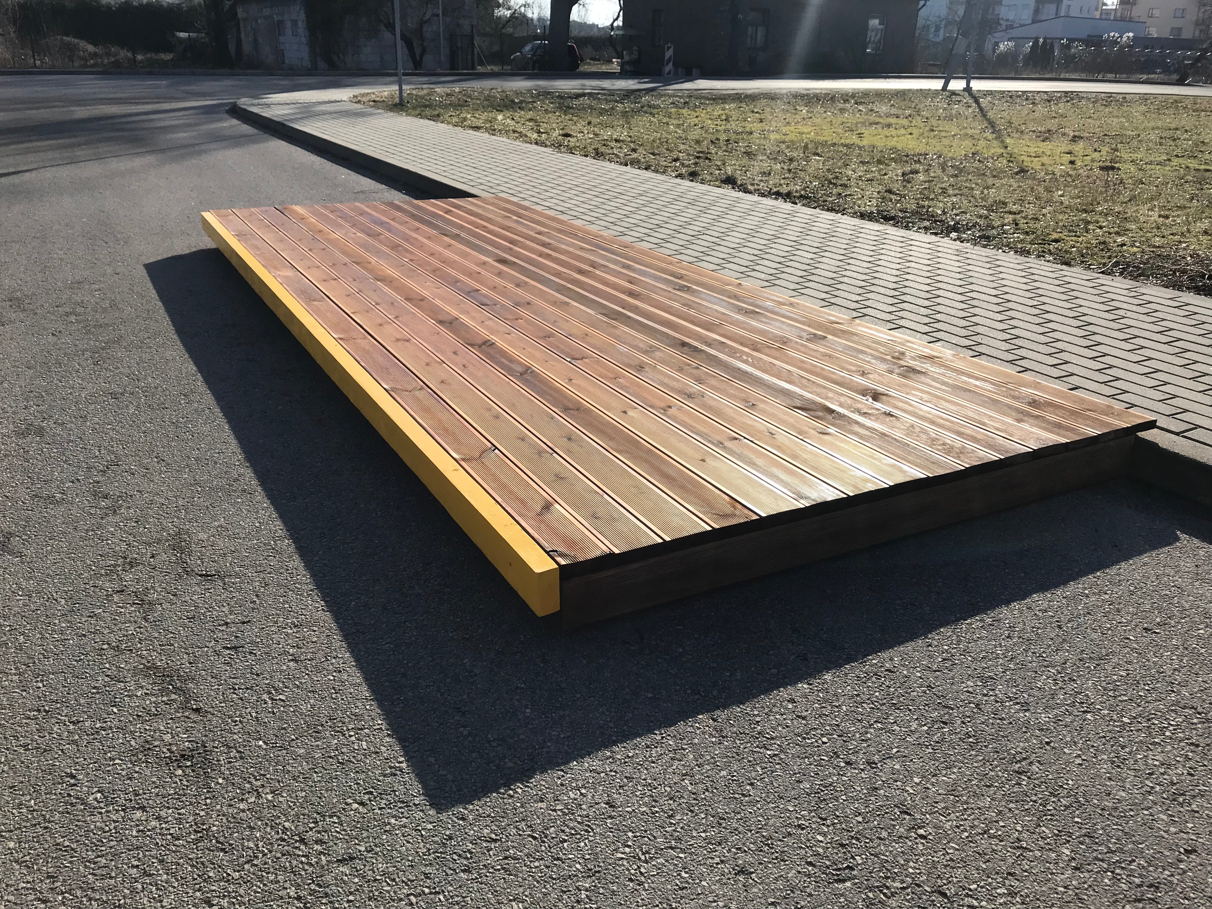 Wooden platform on an asphalt surface with grass and pavement in the background
