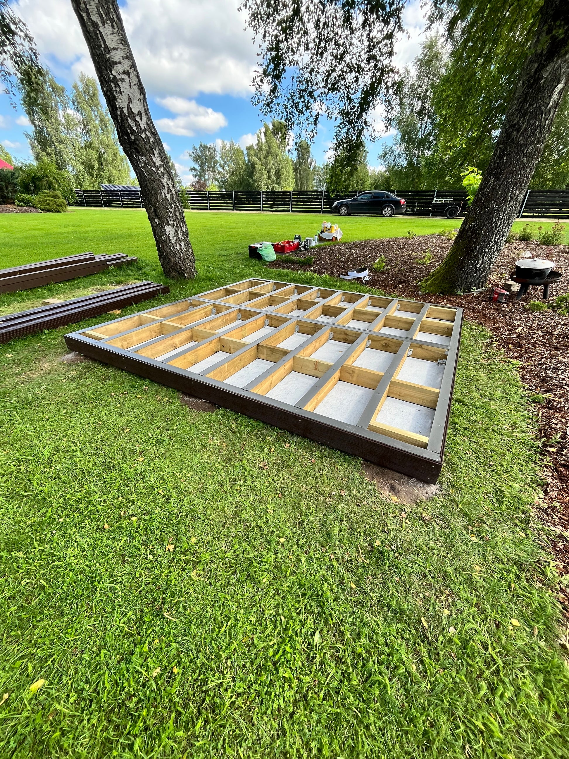 Wooden deck frame on grass with trees and sky in the background