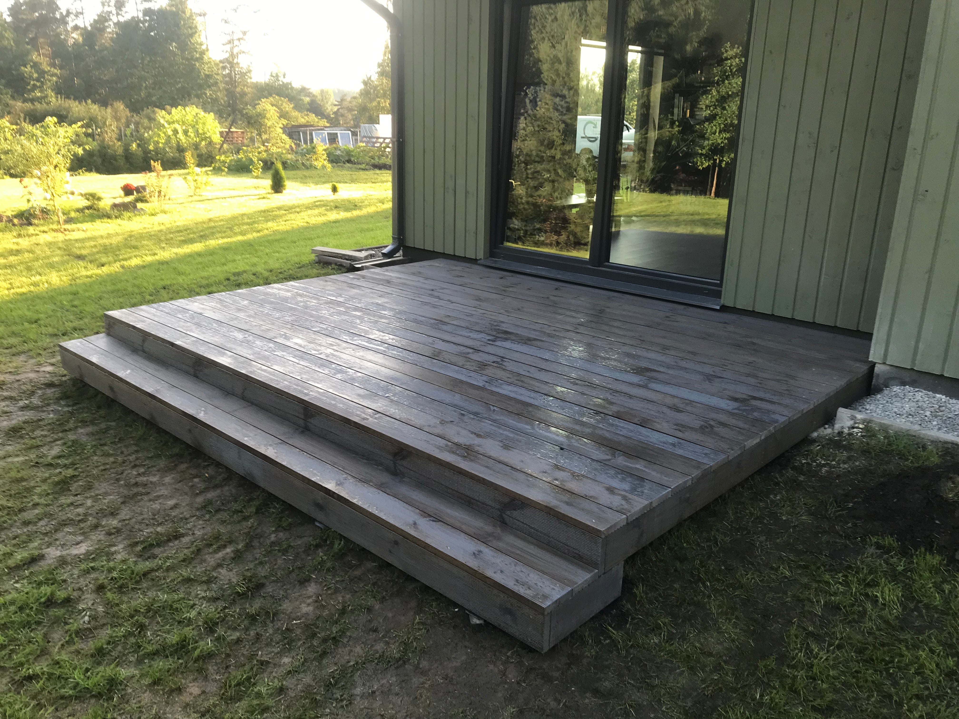 Wooden deck with steps leading up to a house with large windows.