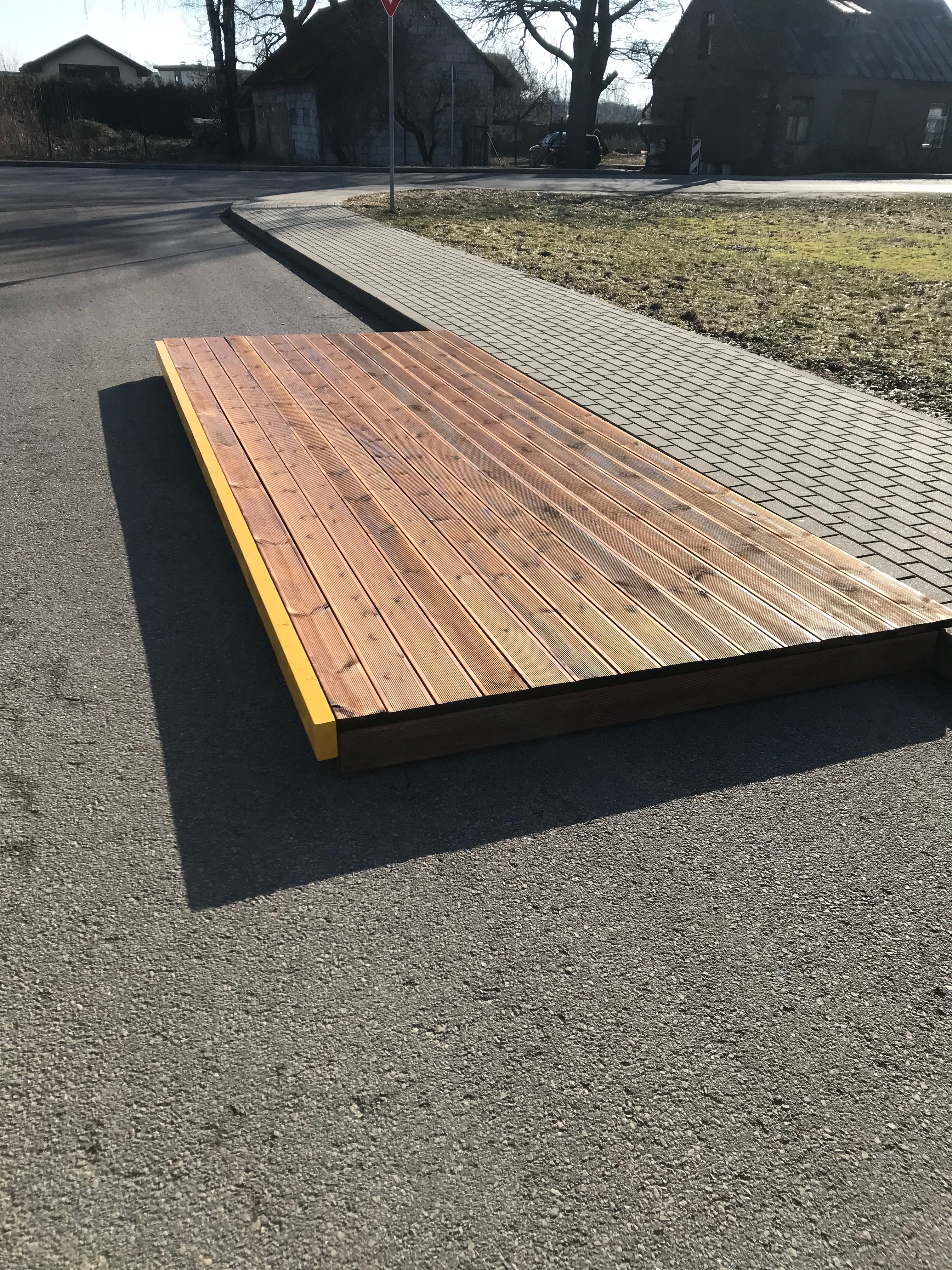 Wooden deck or platform on a street corner with grass and pavement in the background