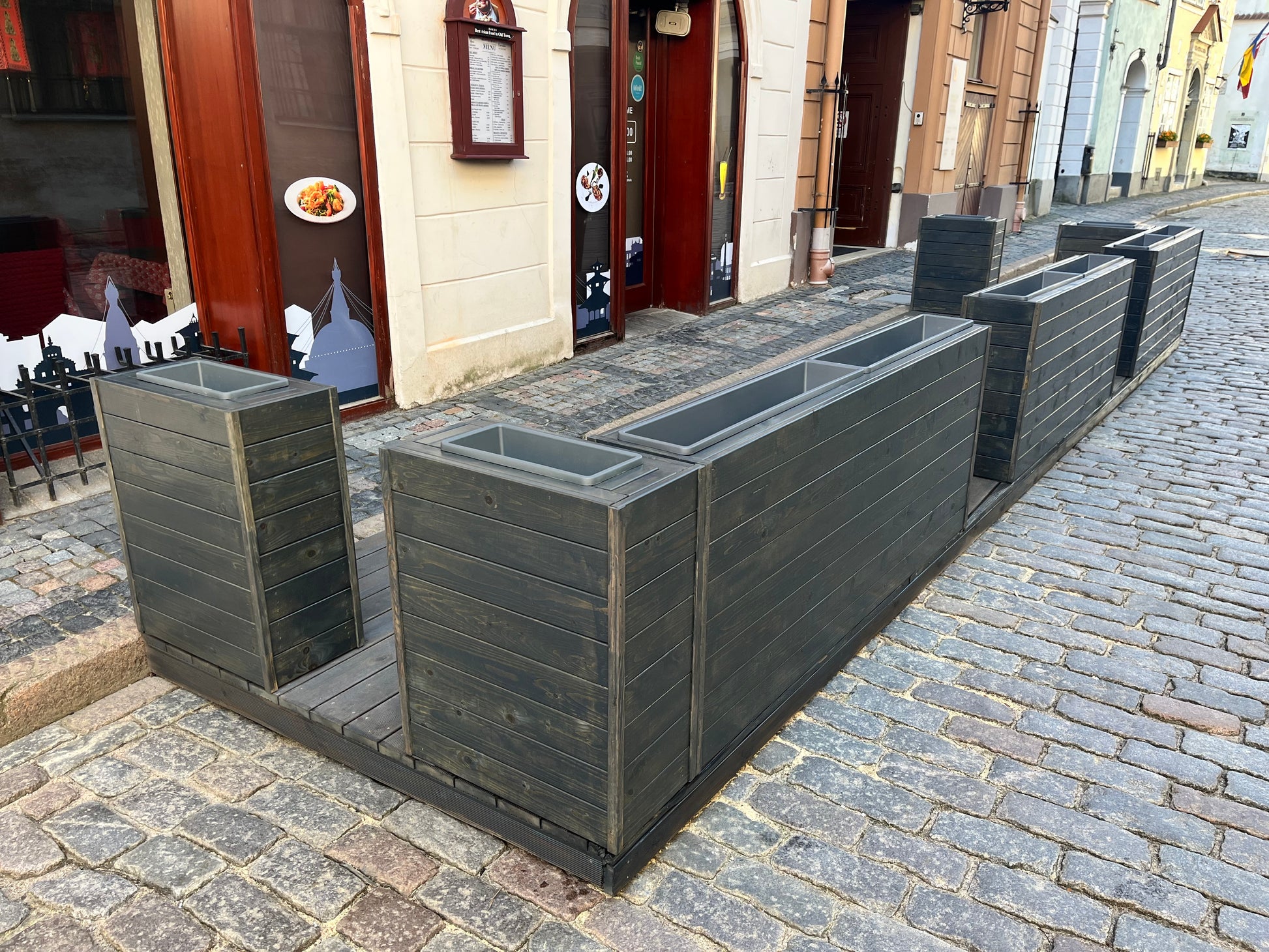 Row of gray rectangular planters on a cobblestone street for restaurant