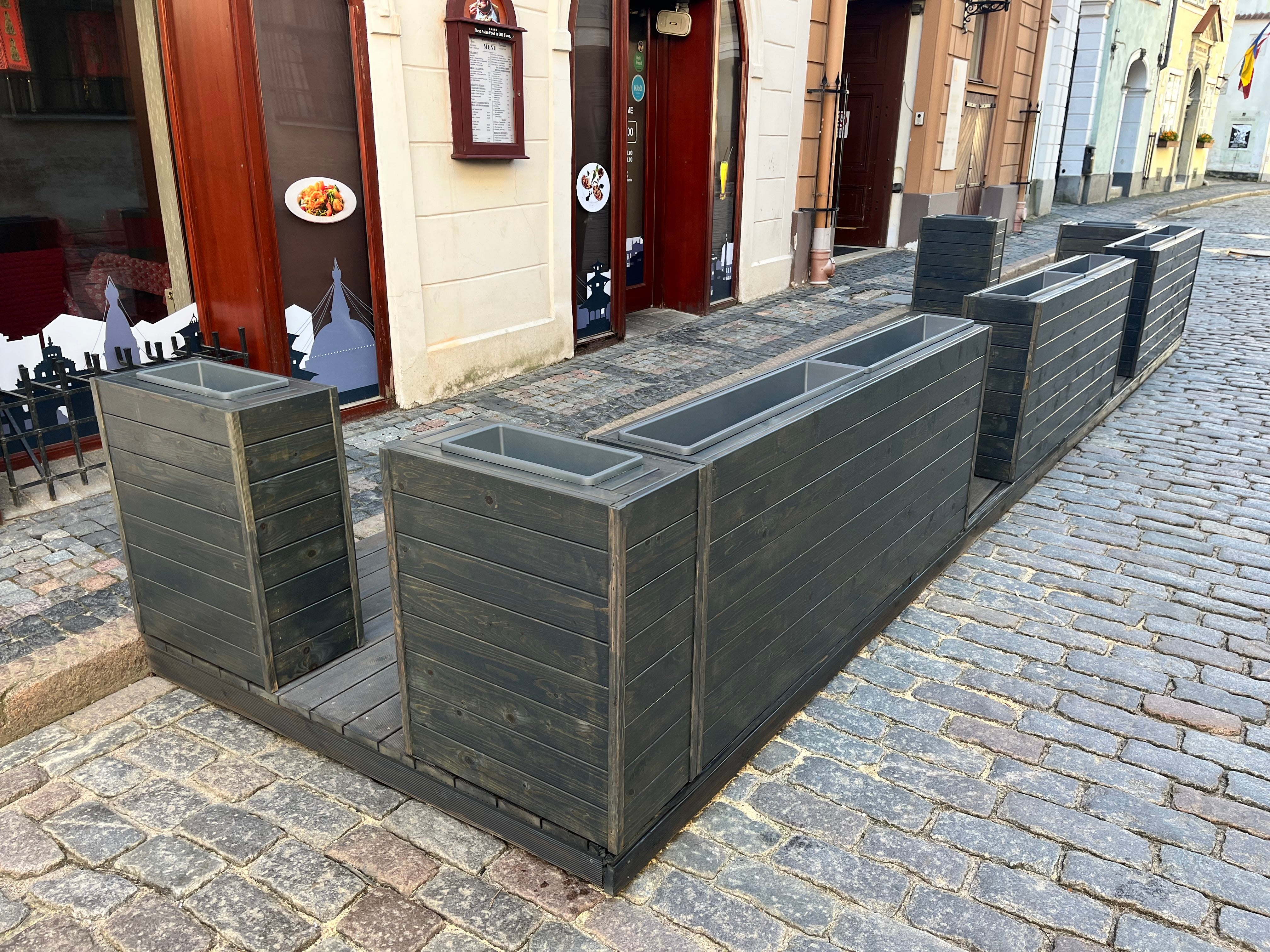 Row of gray rectangular planters on a cobblestone street for restaurant